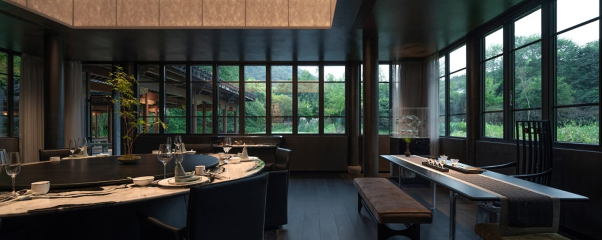A modern dining area with a black table and chairs, surrounded by wine glasses, and natural light from windows