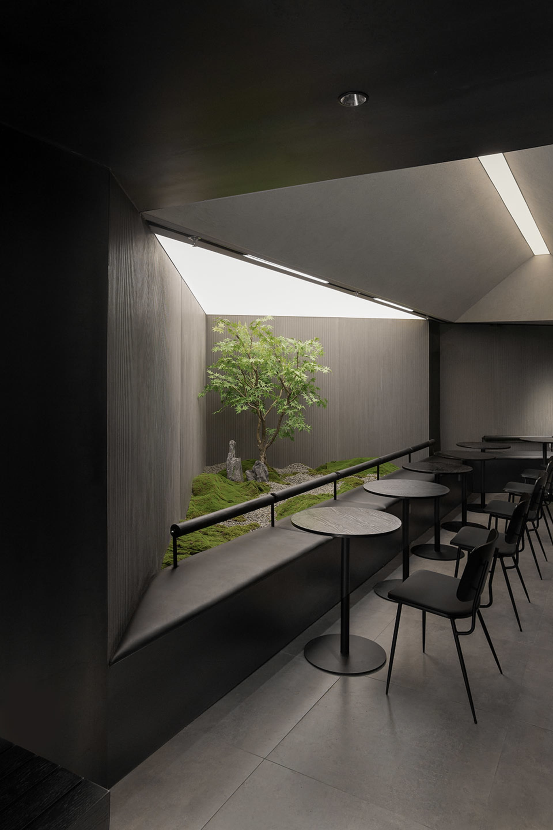 Modern restaurant interior with concrete floors, overhead lamps, and a large dining table, surrounded by chairs and a smaller table in the center