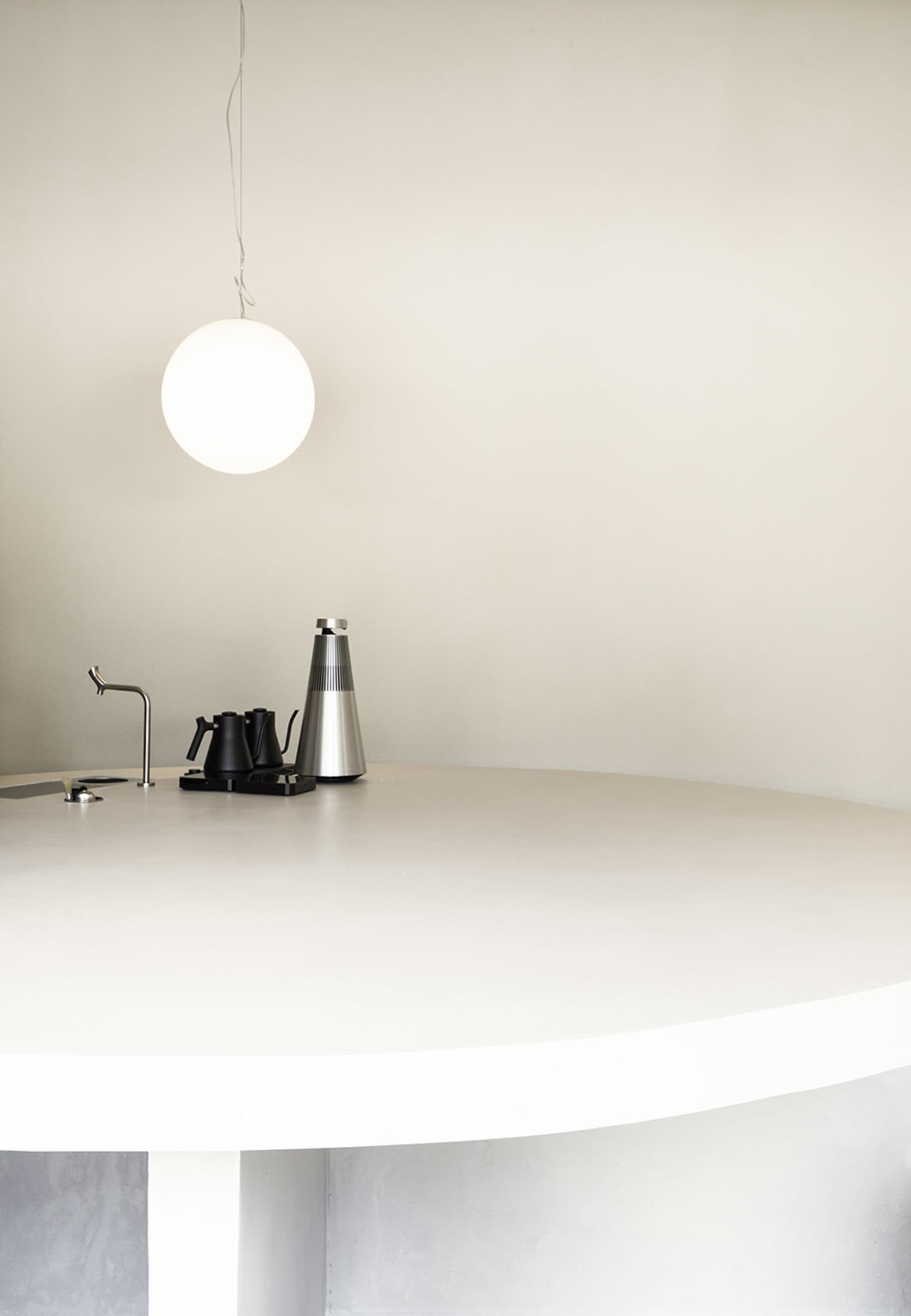 Empty white room with a circular table and two cups, a vase, and minimal decor