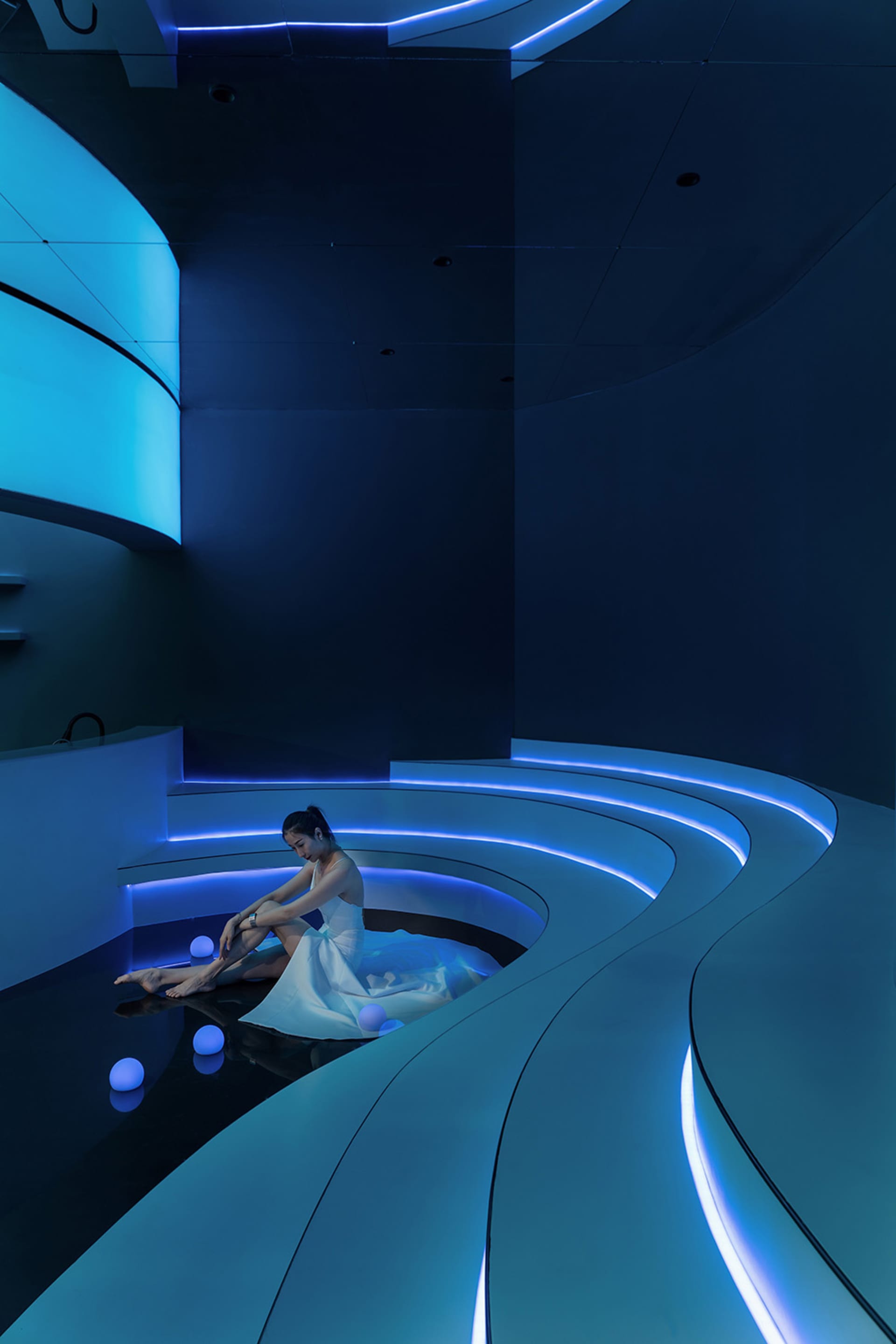 A serene modern bathroom with blue walls, a white bench, and a pool of water, surrounded by balls in a peaceful atmosphere
