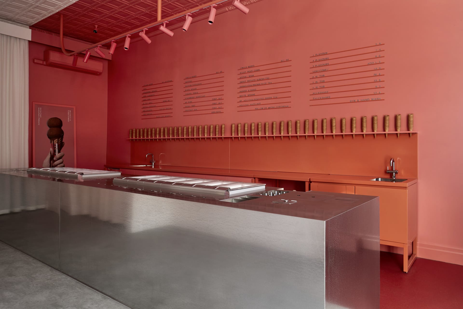 Industrial kitchen with a red accent wall, silver countertops, and multiple ovens and sinks
