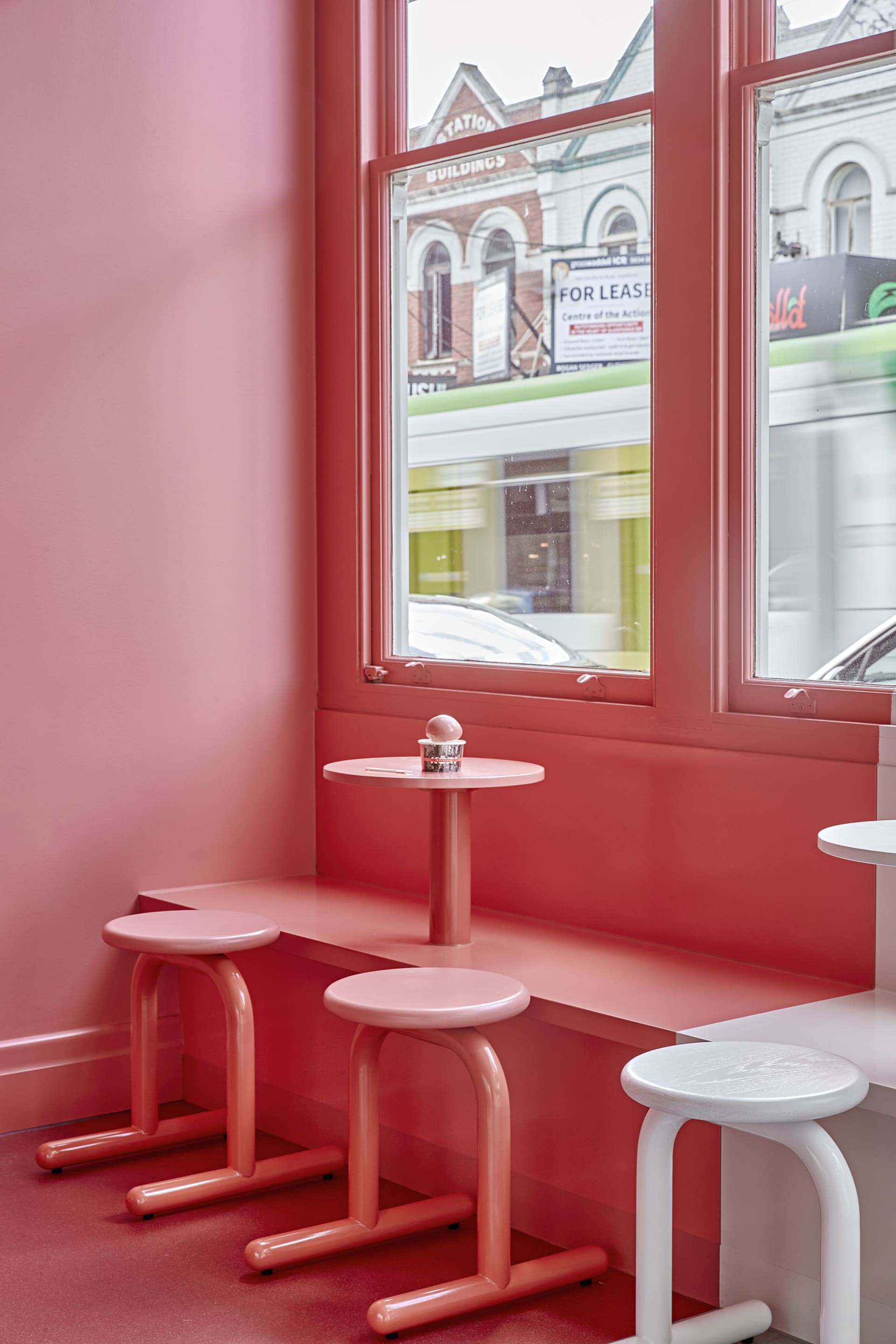 A cozy dining area with red walls, white furniture, and a window with a car visible outside