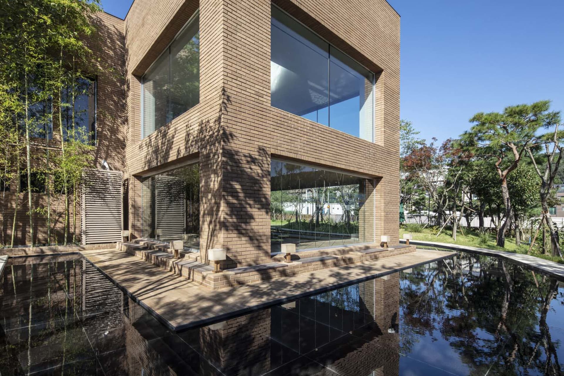 A modern house with a large brick wall and a pool in front, featuring a glass door and several chairs, set in a contemporary style with clean lines and minimalistic elements