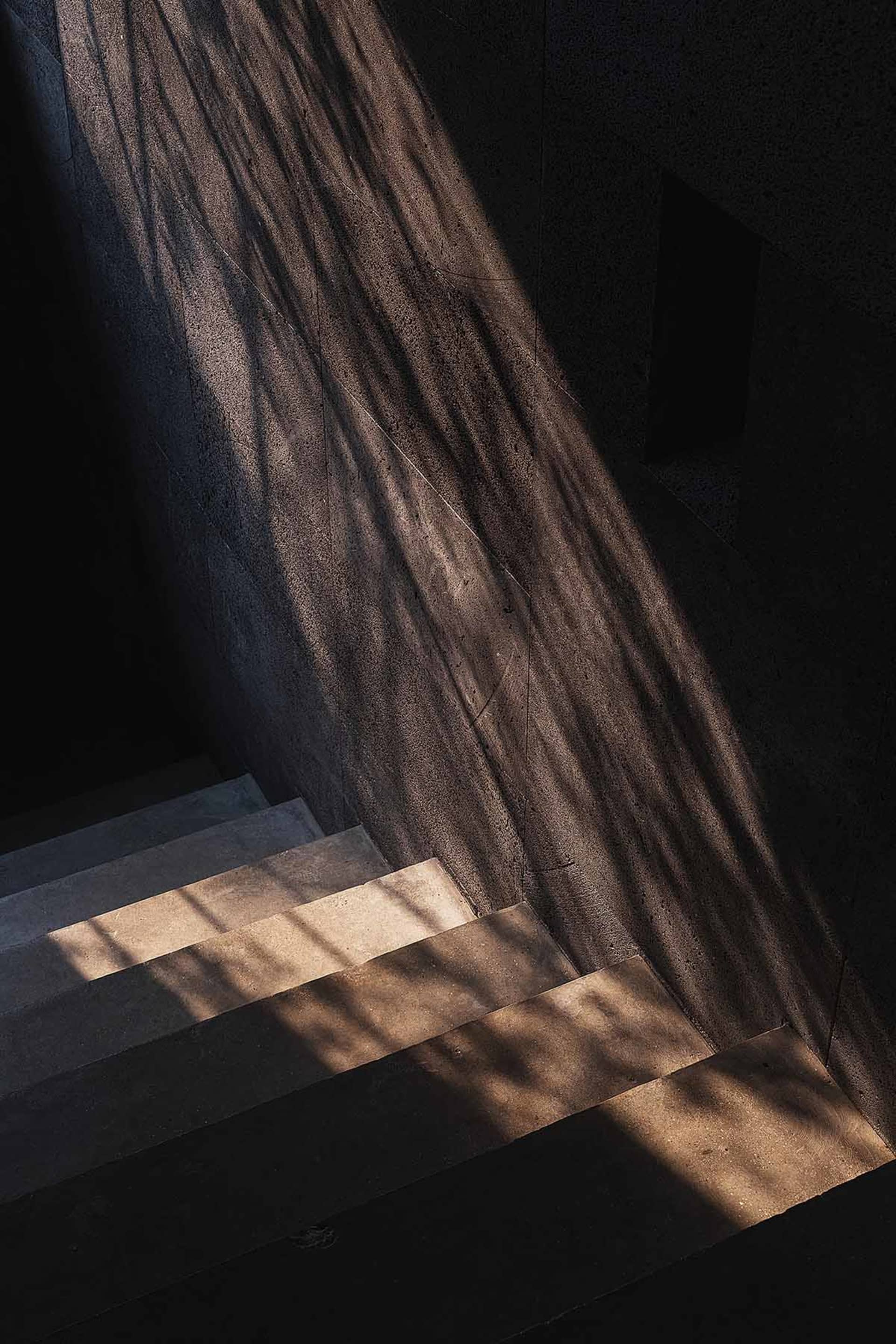 A stone building with a staircase featuring concrete steps and a wooden railing, creating a sense of depth and complexity