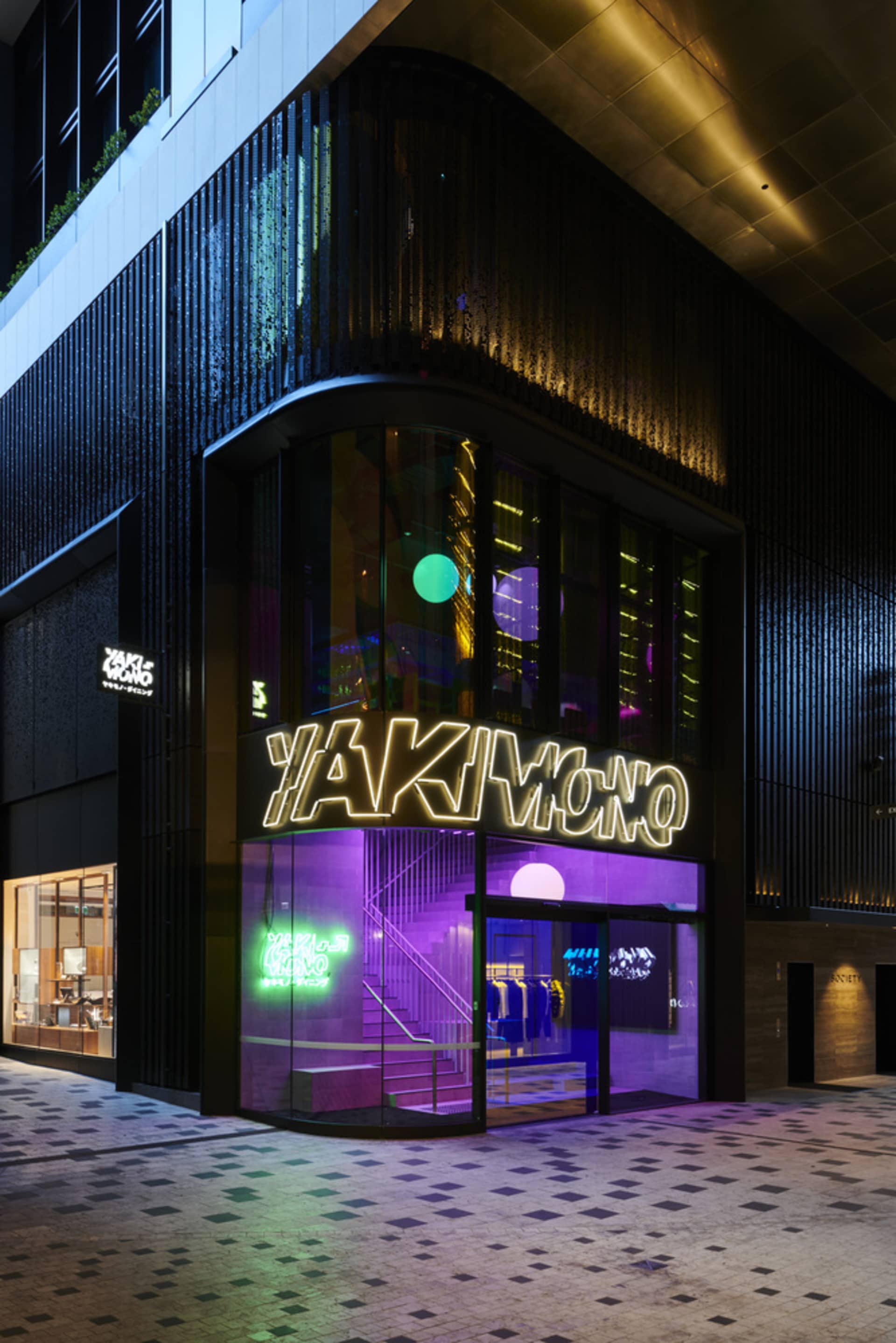 A bustling city street at night with a large building featuring a purple neon sign, surrounded by other signs and bright lights