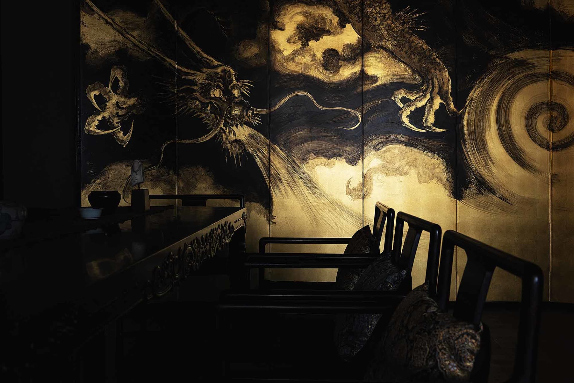 A cozy Asian restaurant interior with a wooden dining table surrounded by chairs and black seats, creating an intimate dining experience