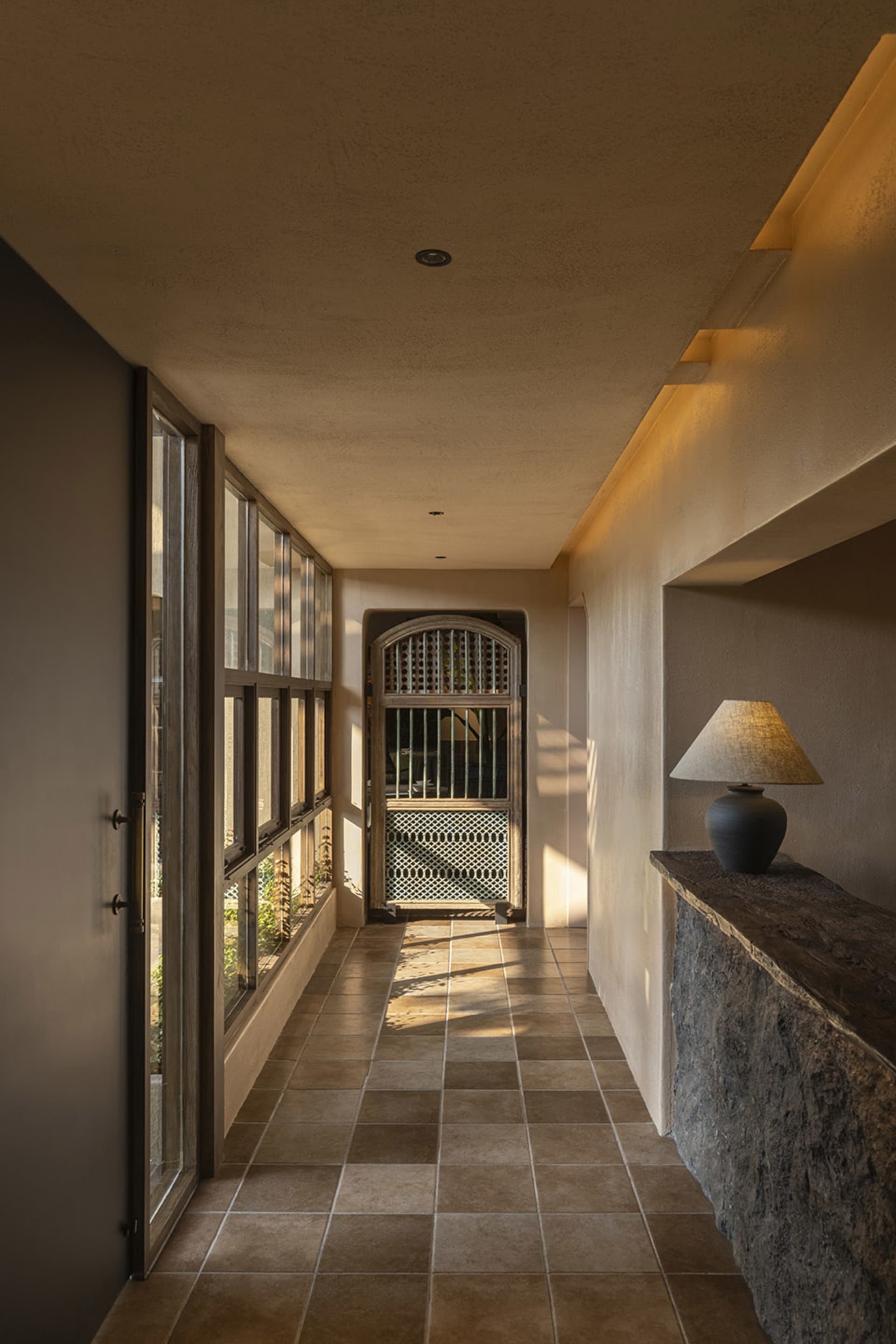 A warm and inviting interior hallway with a stone wall and tile flooring, lit by natural light from two windows on either side