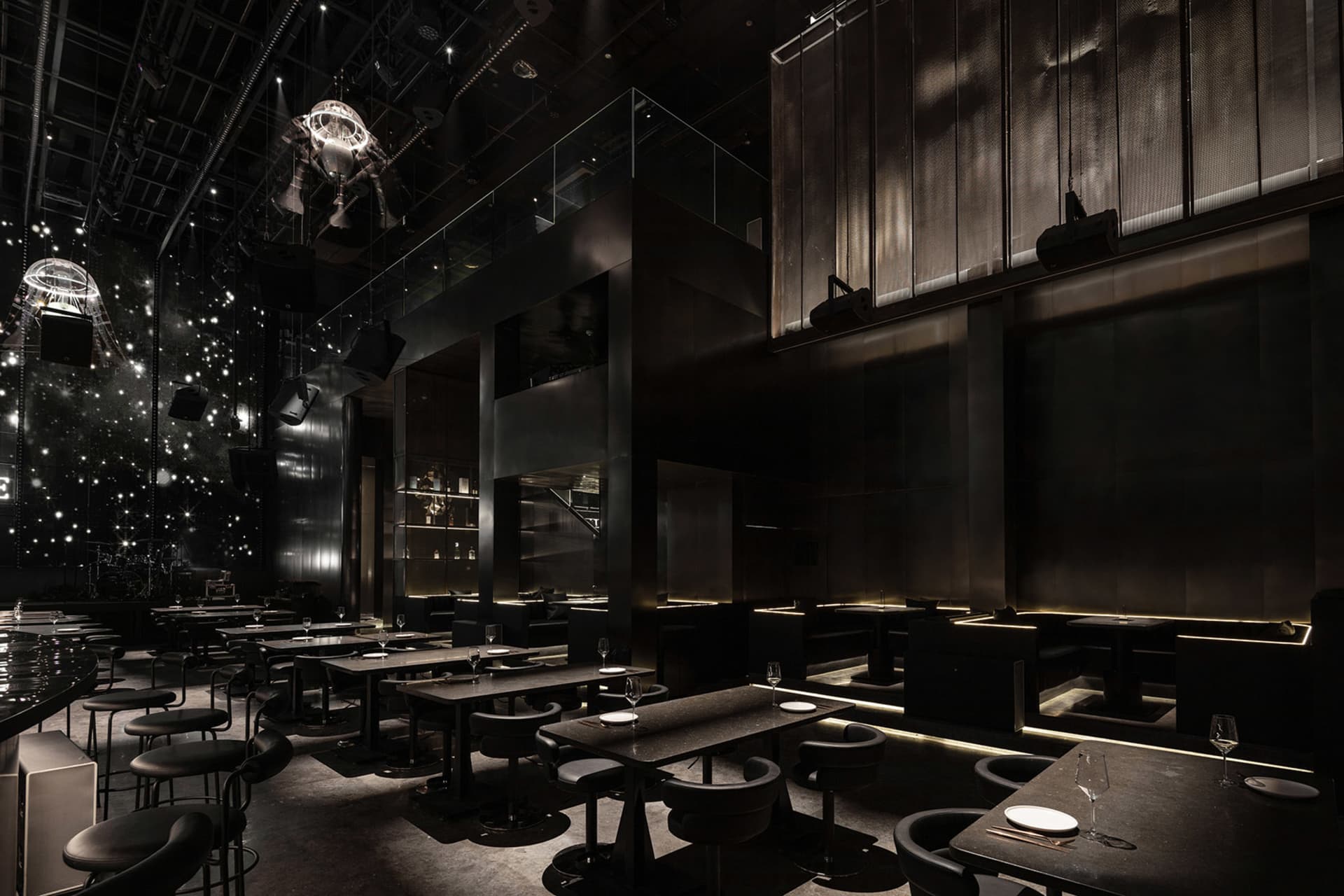 Dark and intimate restaurant interior with multiple dining tables, chairs, and wine glasses, creating a cozy ambiance