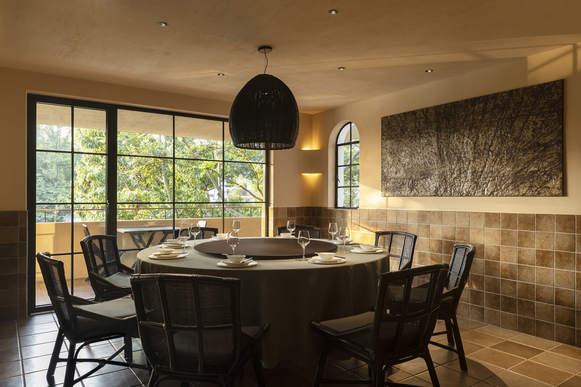 A cozy dining area with a round table, chairs, and wine glasses, surrounded by tile walls and warm lighting