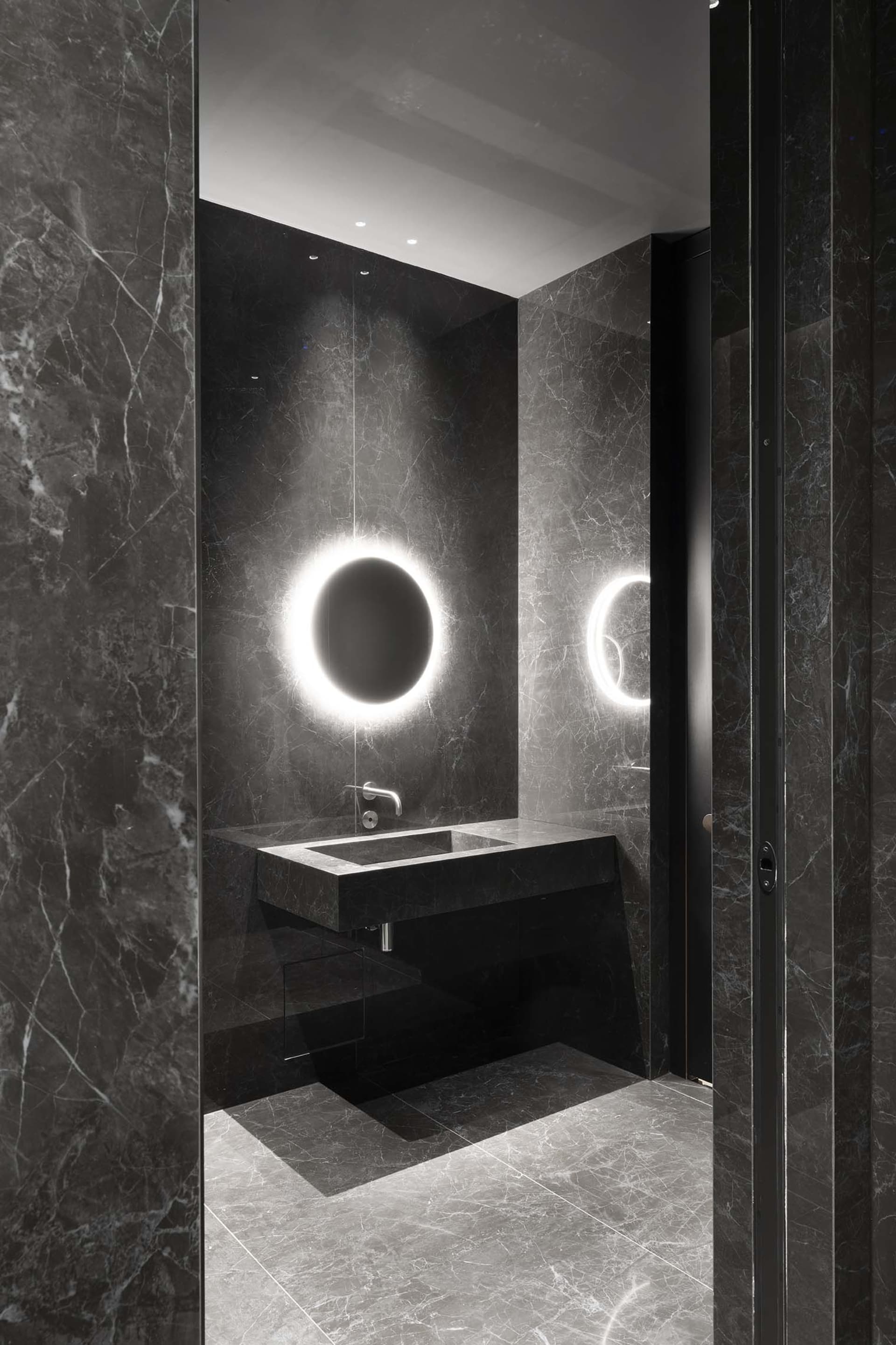 Modern bathroom with a sink, mirror, and shower area, featuring black marble flooring and sleek design