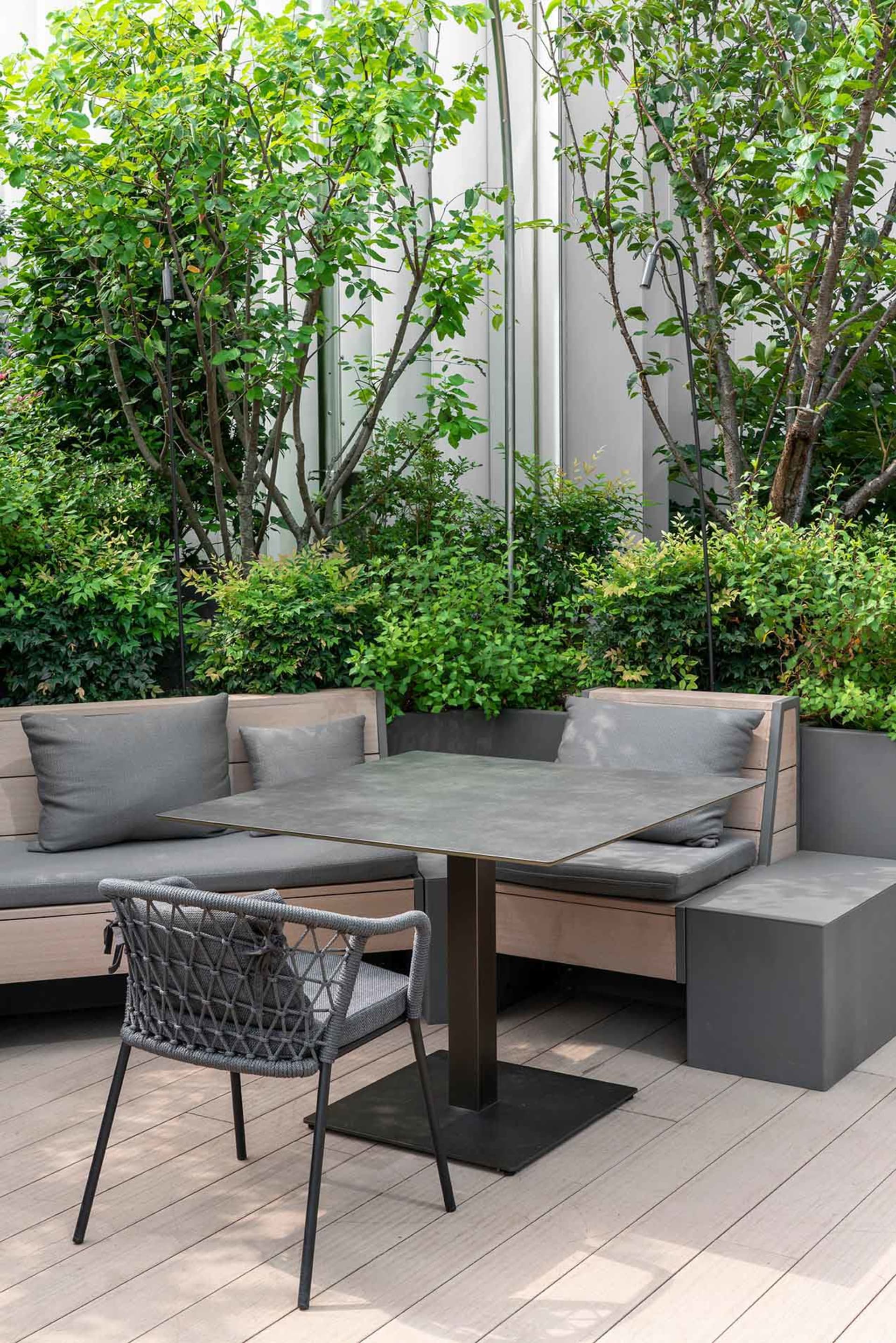 A wooden dining table with a metal base is surrounded by three chairs in a comfortable outdoor seating arrangement