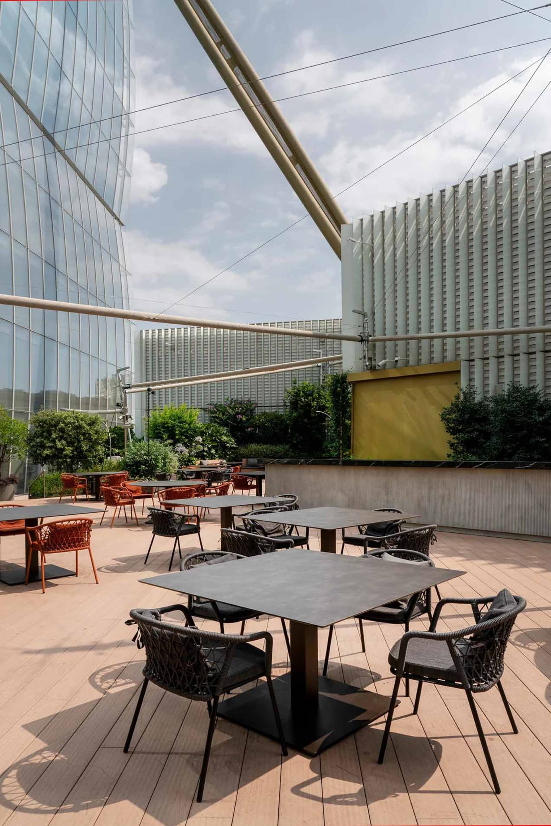 A patio area with multiple dining tables and chairs, surrounded by natural light, creating a comfortable and inviting atmosphere