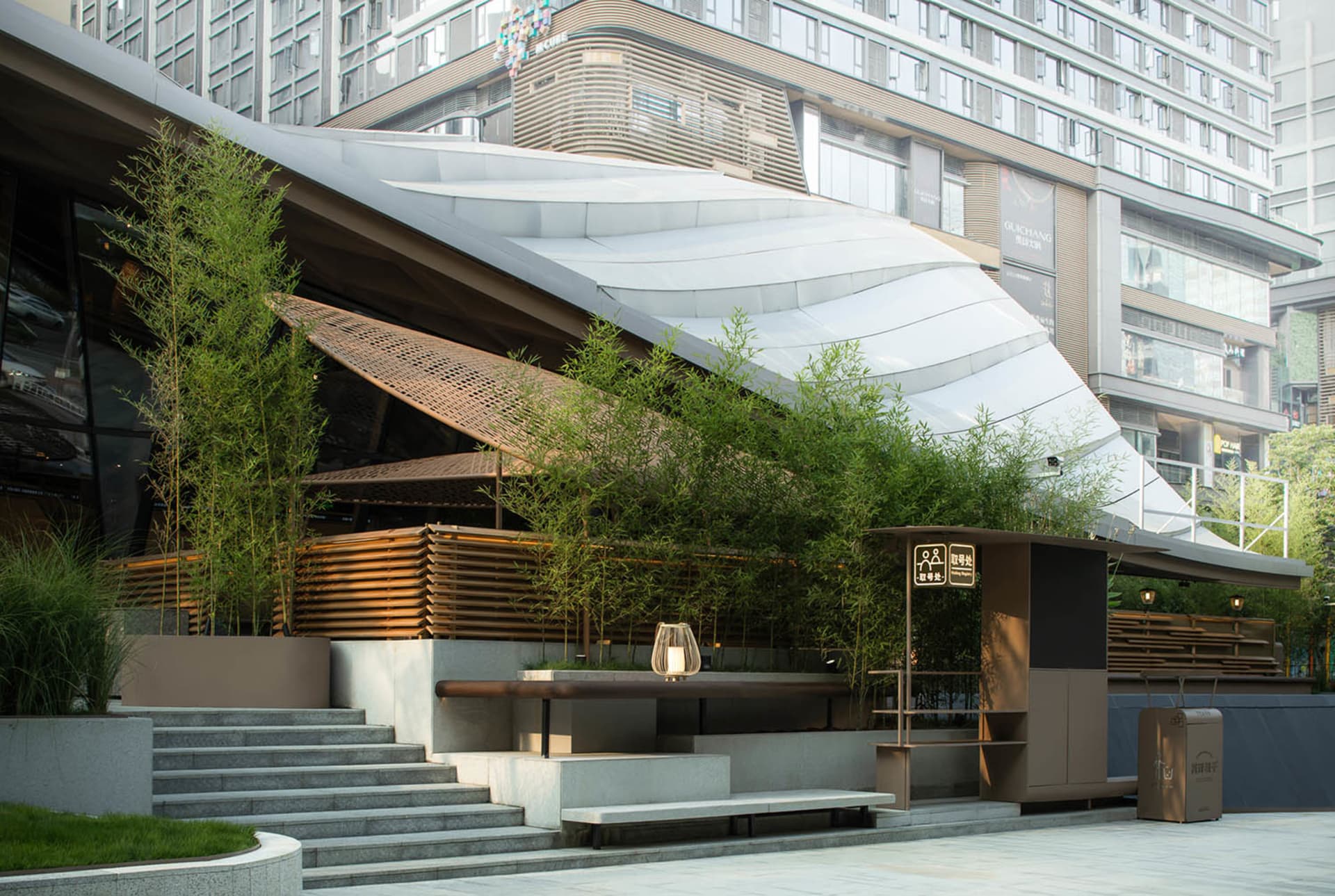 A modern building with a curved glass roof and potted plants in various sizes and positions around the exterior