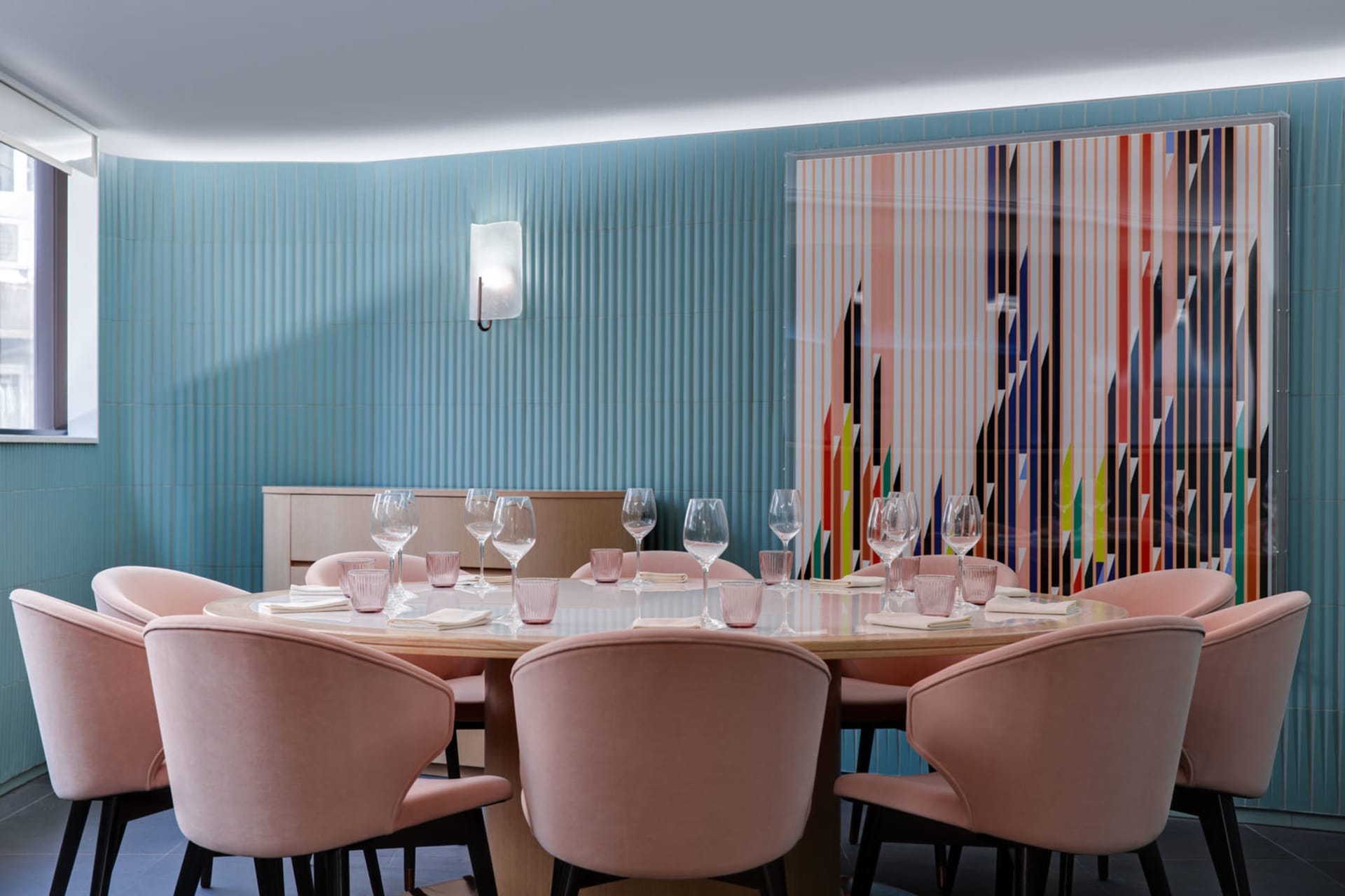 A dining area with a long pink table set for a meal, surrounded by chairs and wine glasses, creating a warm and inviting ambiance