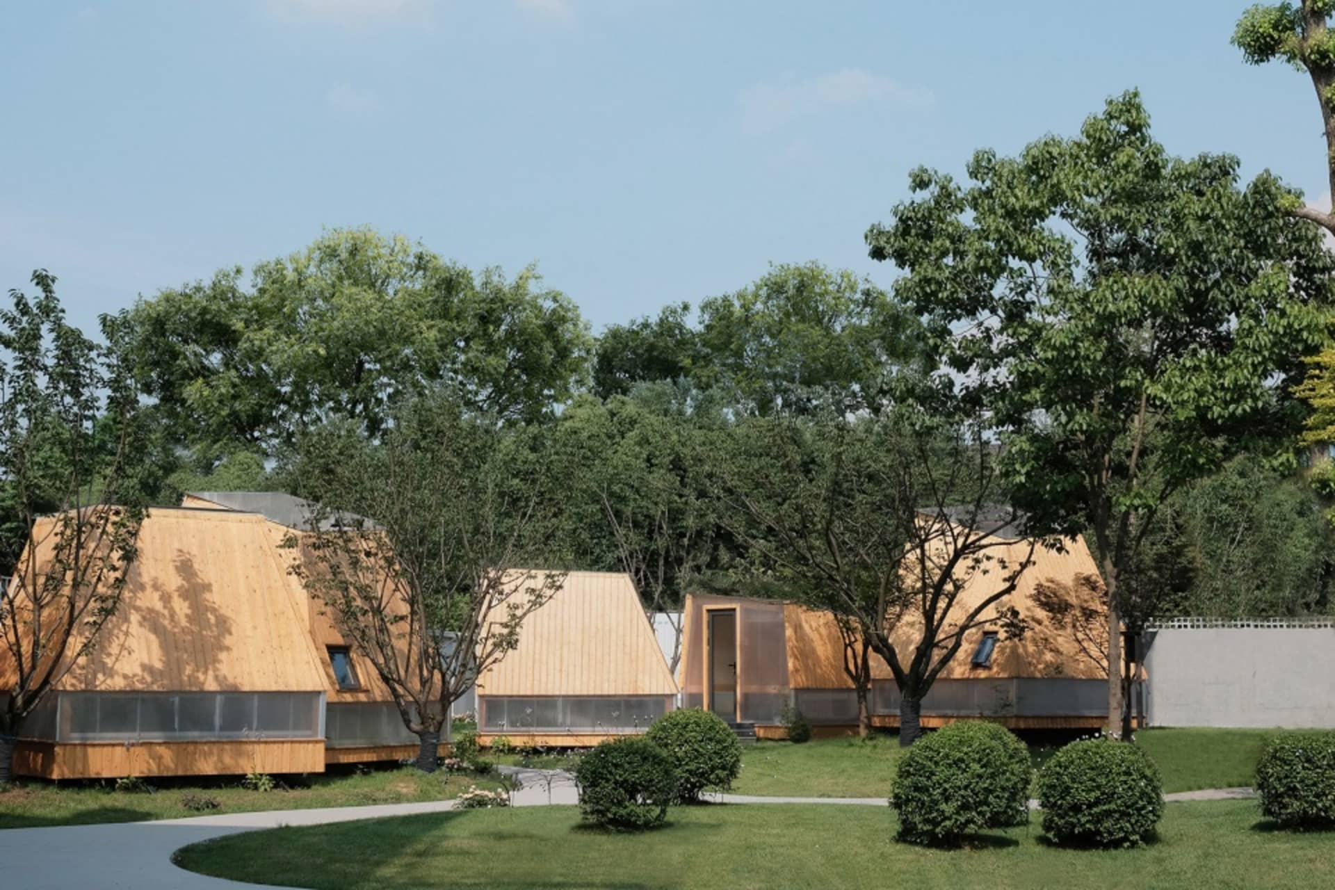 A row of wooden houses in a grassy area surrounded by trees, conveying a sense of tranquility and harmony between nature and architecture