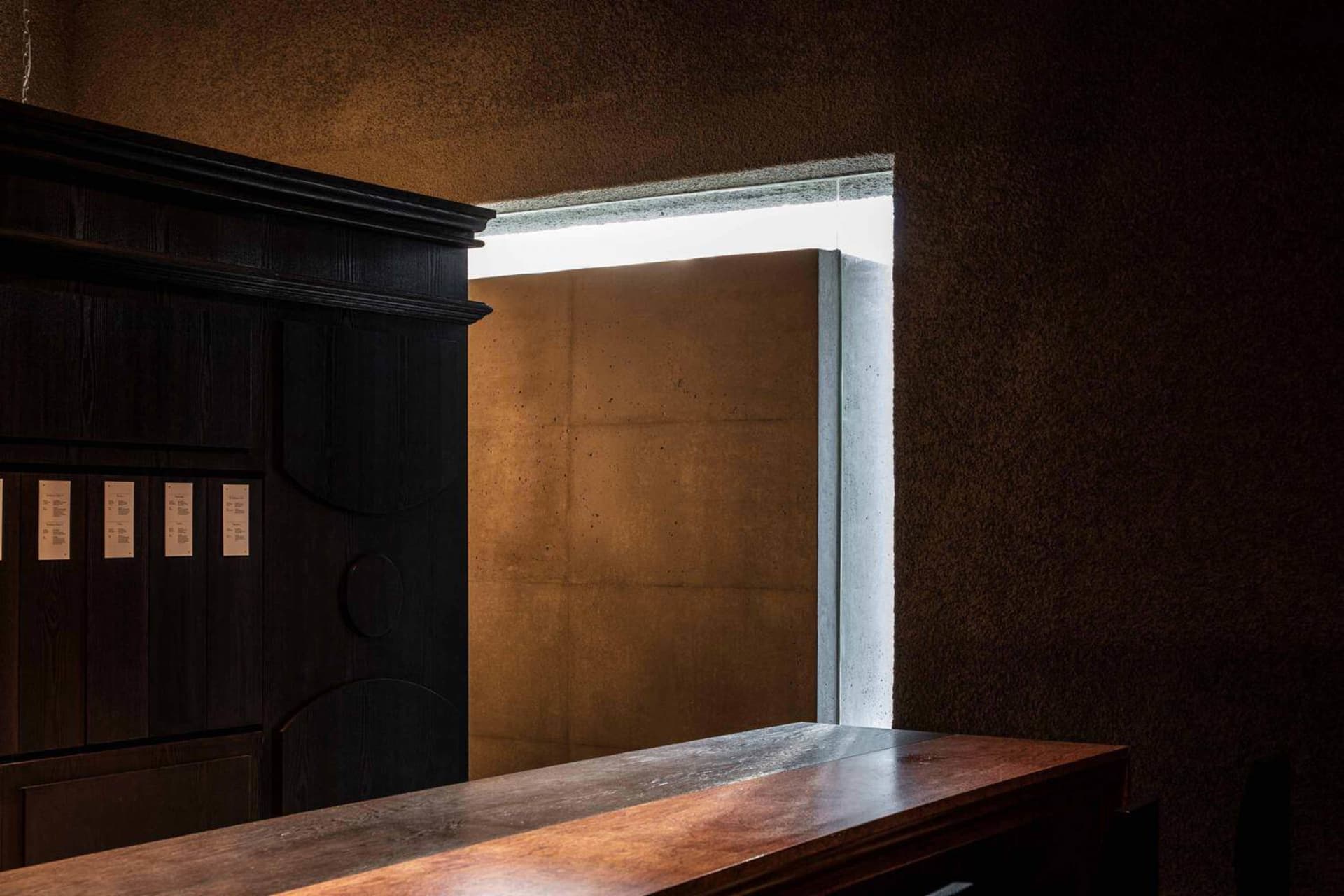 Dimly lit room with a wooden cabinet, concrete walls, and natural light from two windows
