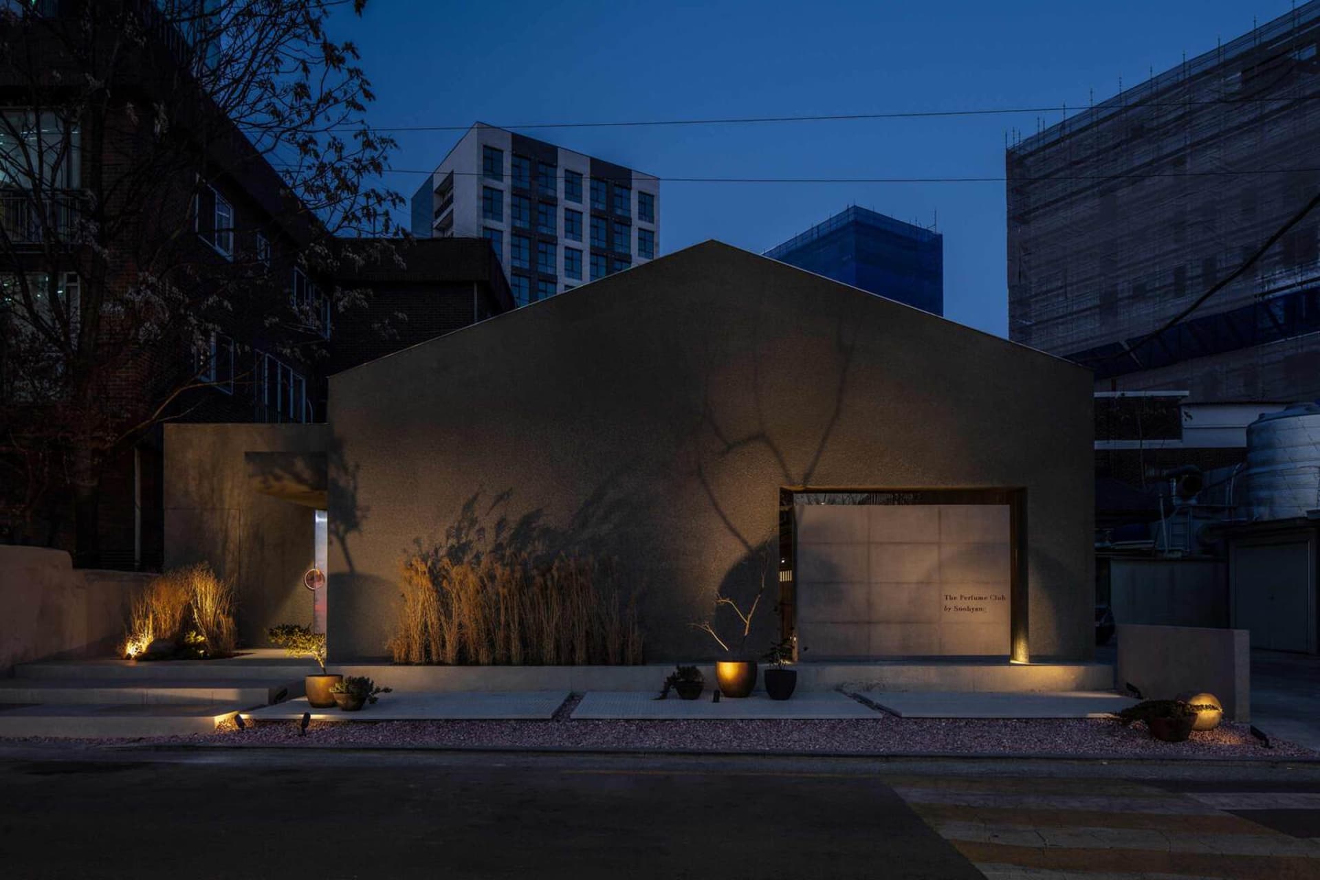 A modern building with a prominent archway and potted plants, set against a calm night sky