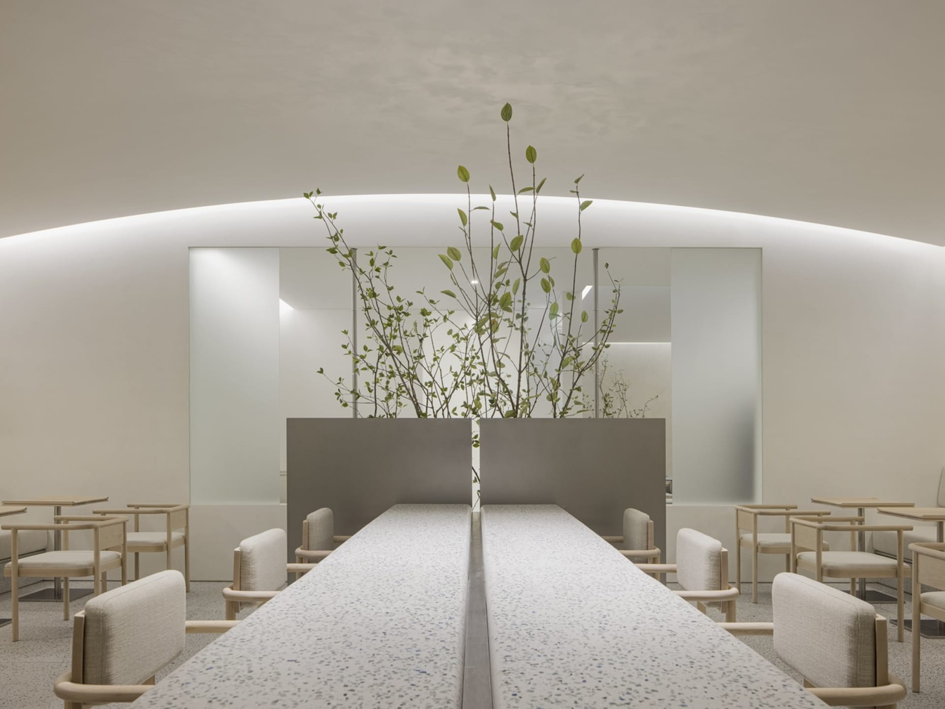 A clean and inviting restaurant interior with a long dining table, chairs, and potted plants