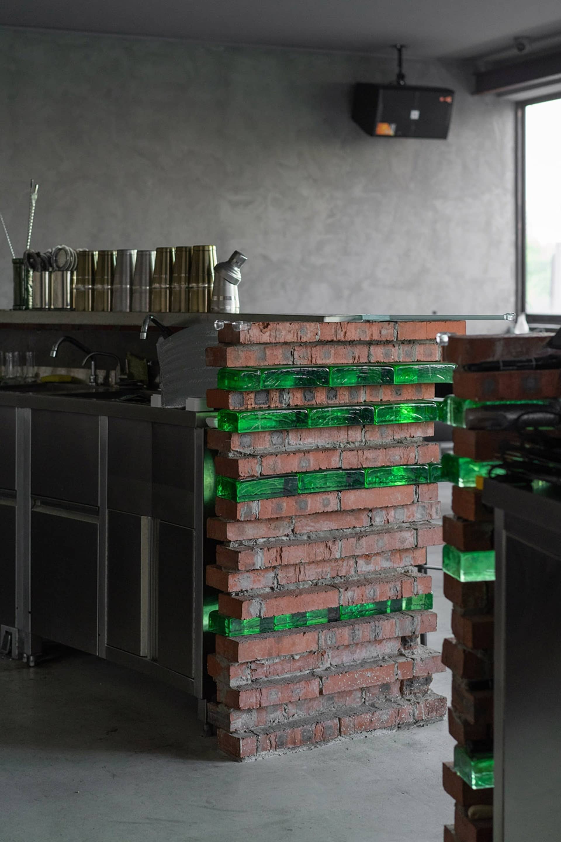 Industrial kitchen with a brick wall, two sinks, and various bottles and cups scattered around the space