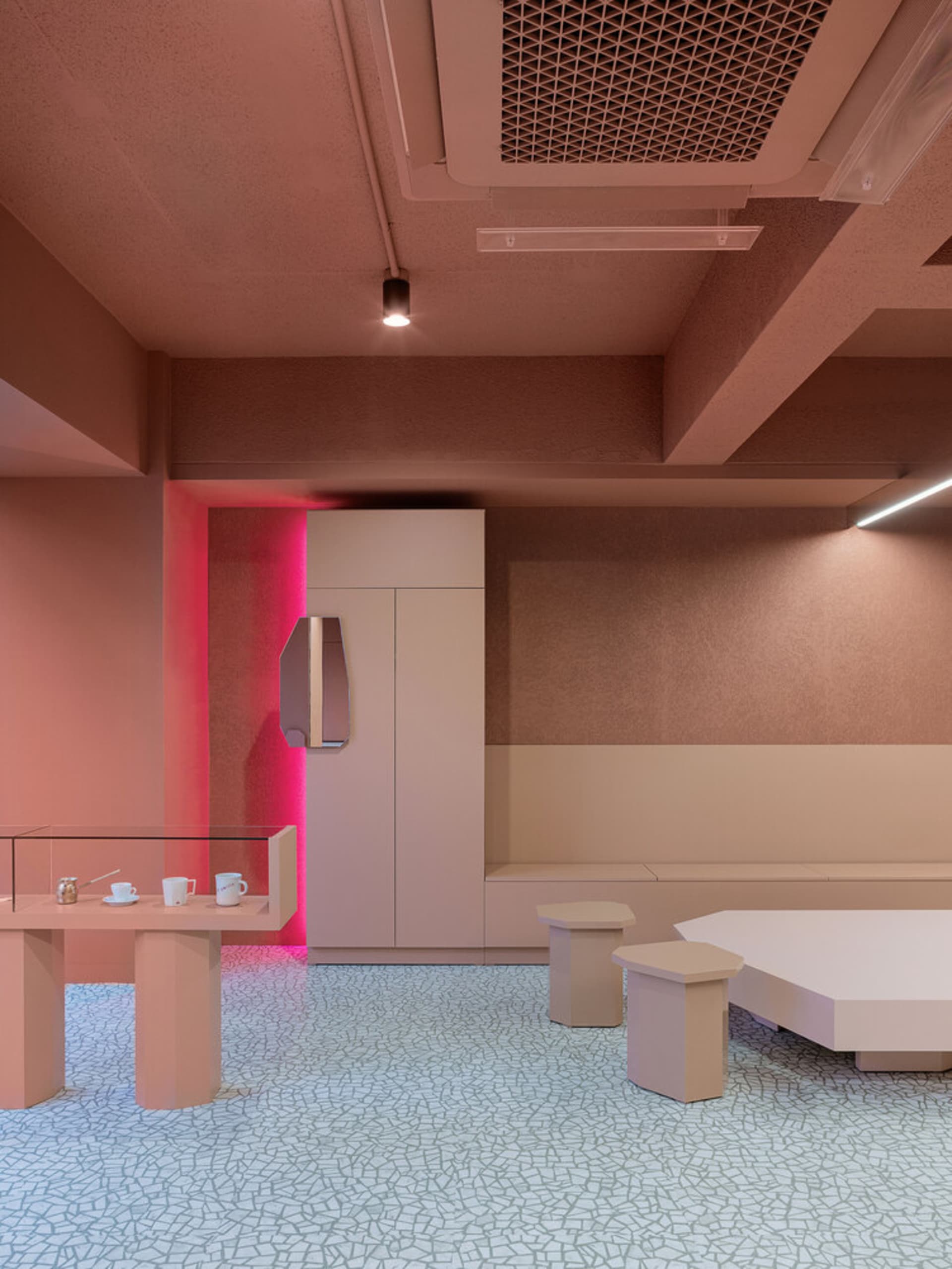 A modern cafe with pink accents, tables, chairs, and a refrigerator, conveying a welcoming atmosphere