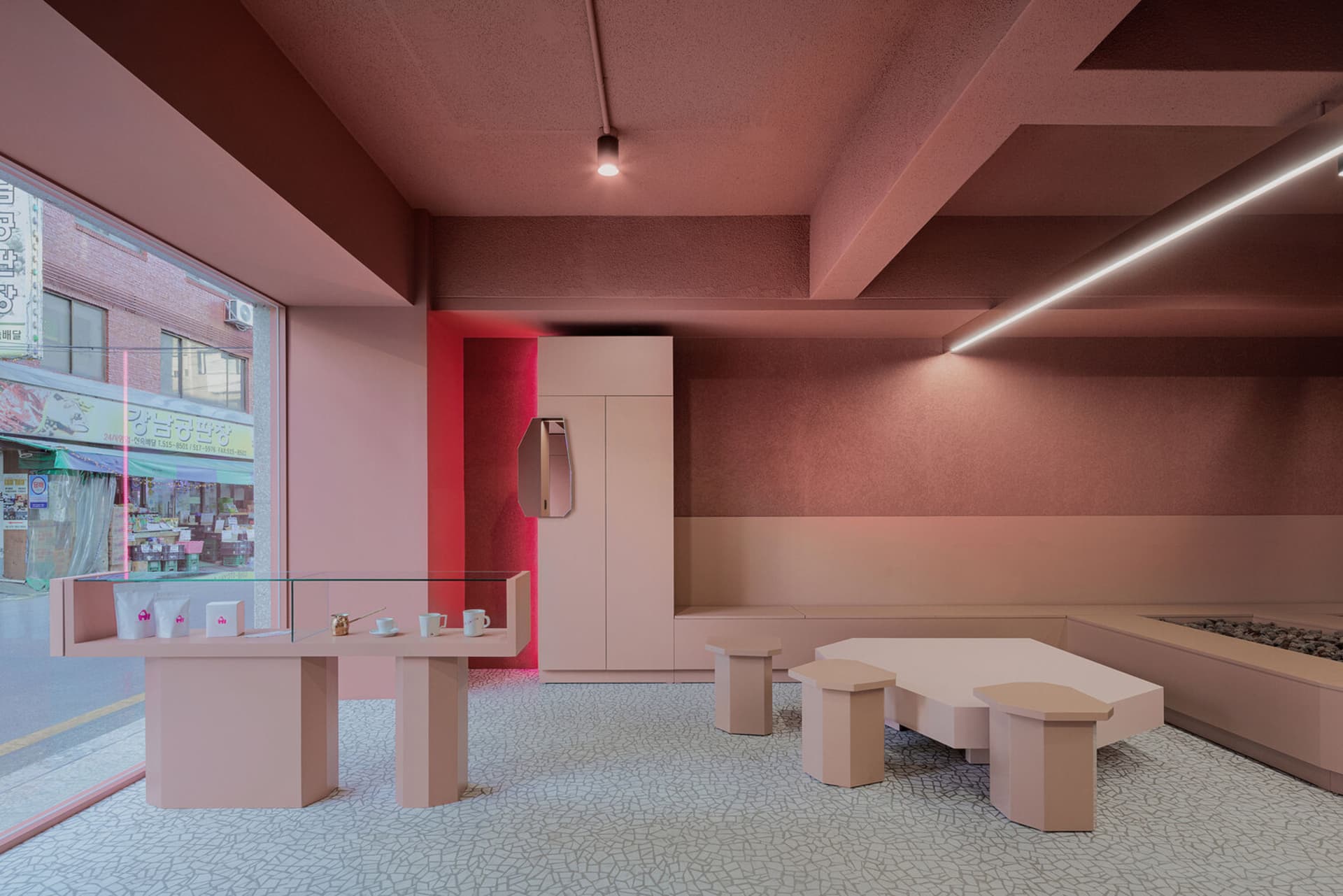 A cozy dining area with pink walls, tiled flooring, and multiple tables and chairs, featuring a refrigerator and ample seating options