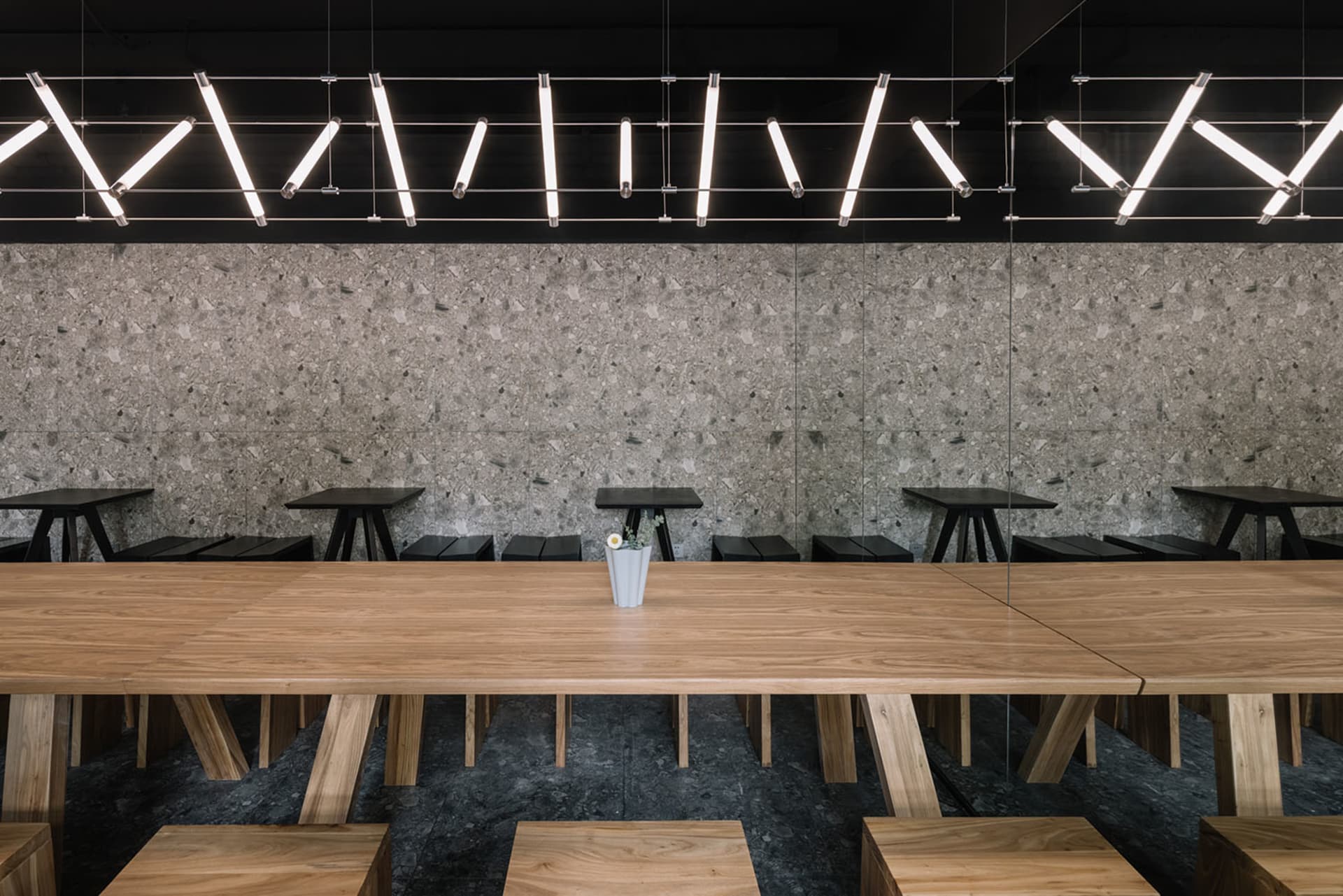 A modern restaurant interior with a large wooden dining table surrounded by multiple chairs, featuring a warm and inviting ambiance with natural materials and clean lines