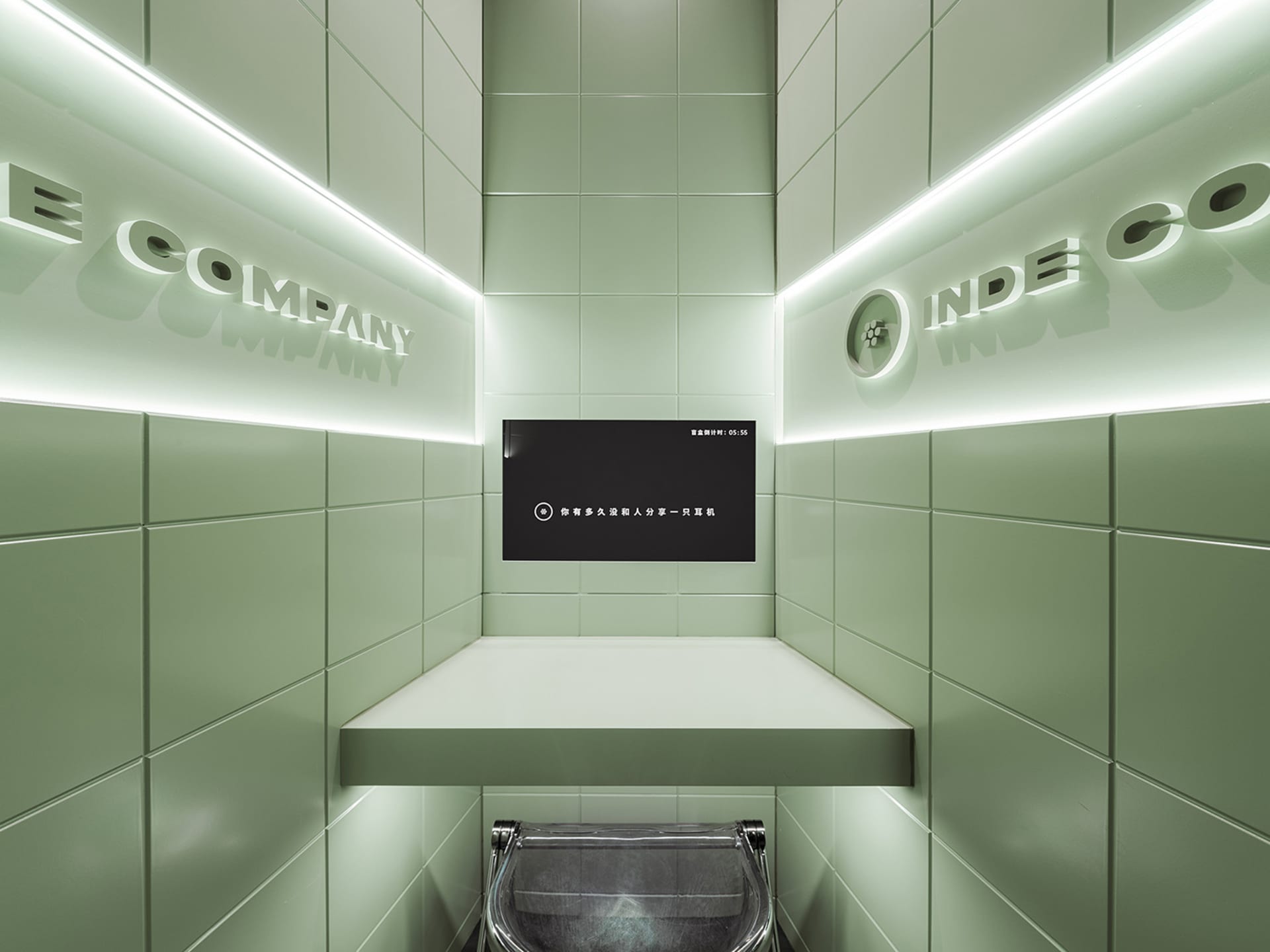 Bathroom with green tiles, two sinks, and a TV above one sink, in a well-lit space