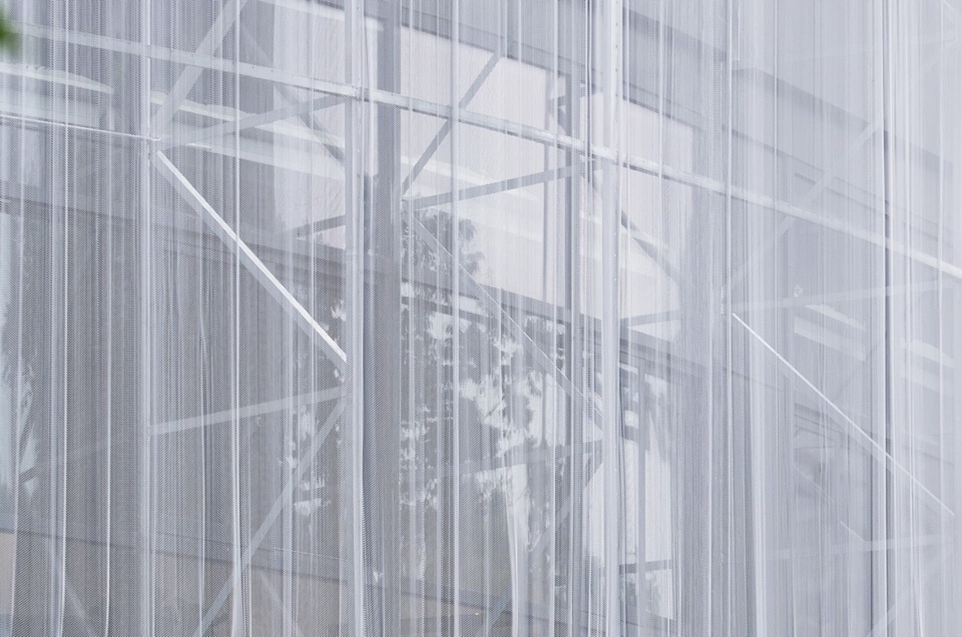 A modern office building with a concrete facade, large windows, and a mesh-like structure covering the glass for privacy