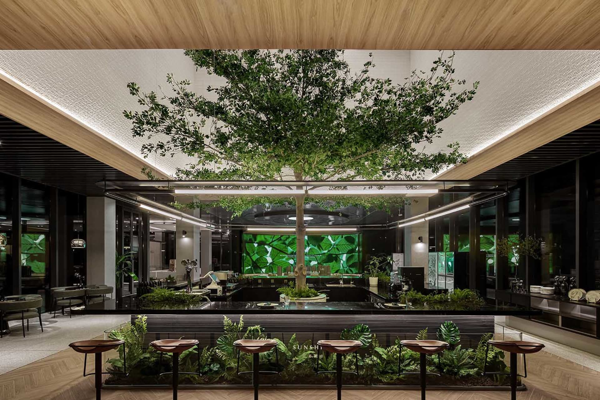 A large lobby with a central tree, chairs, and dining tables, creating an inviting and comfortable atmosphere with natural elements