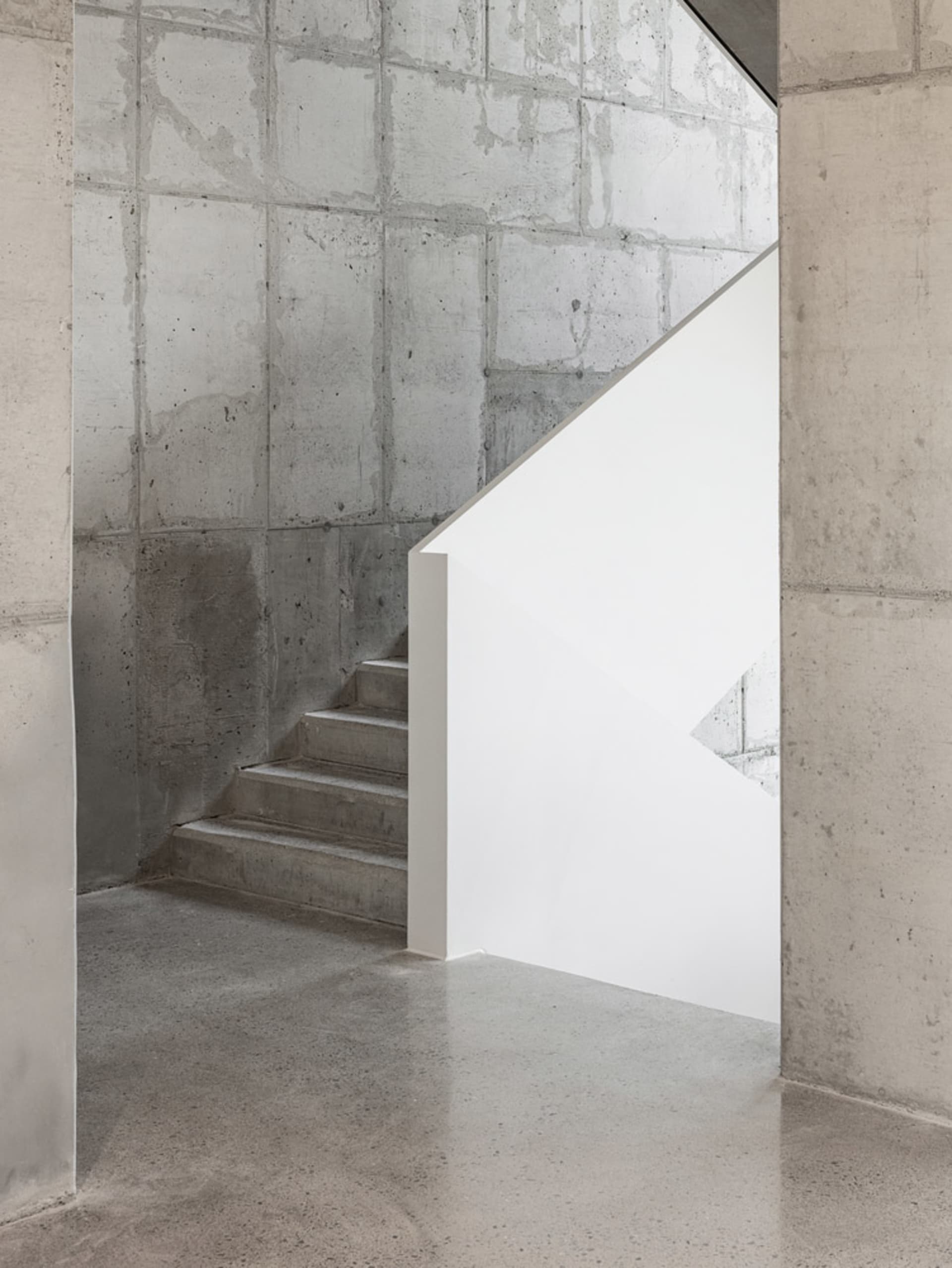A photo of a staircase in a building with concrete stairs and a wall, suggesting a functional yet plain interior design
