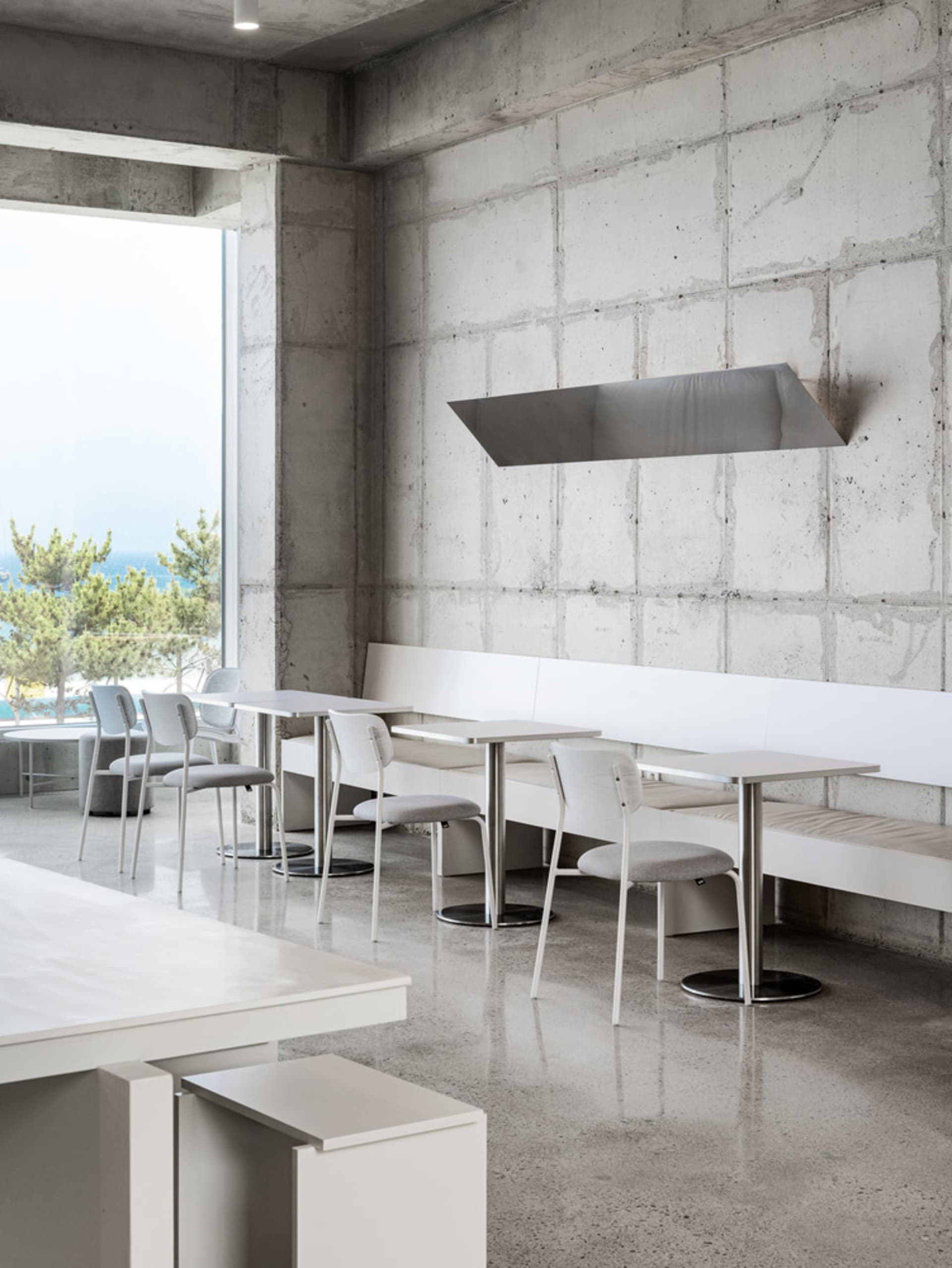 A modern restaurant interior with multiple dining tables and chairs, concrete walls, and a focus on functionality and clean lines