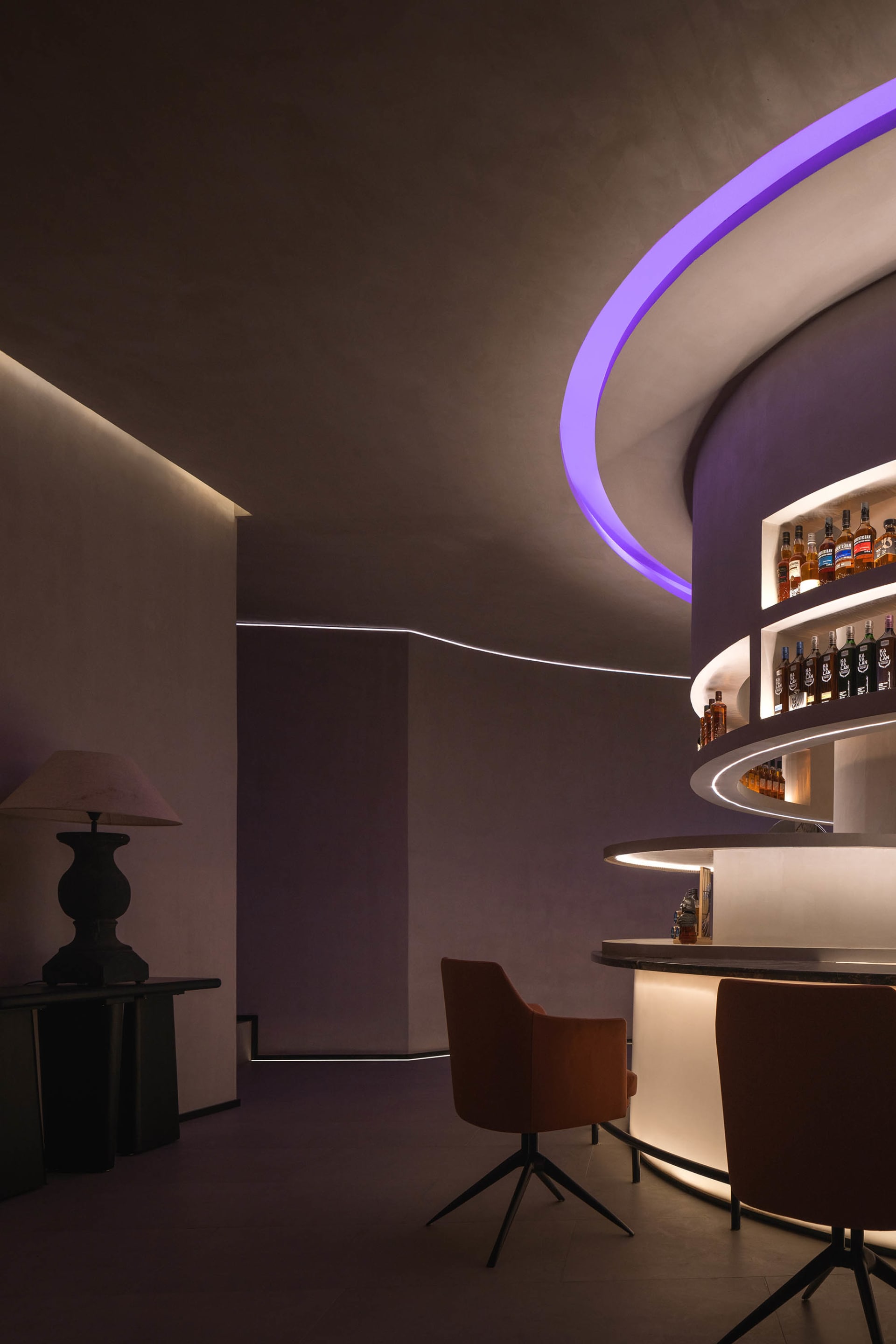 Modern bar area with a circular counter, two chairs, and a display of bottles, set in a stylish and functional space