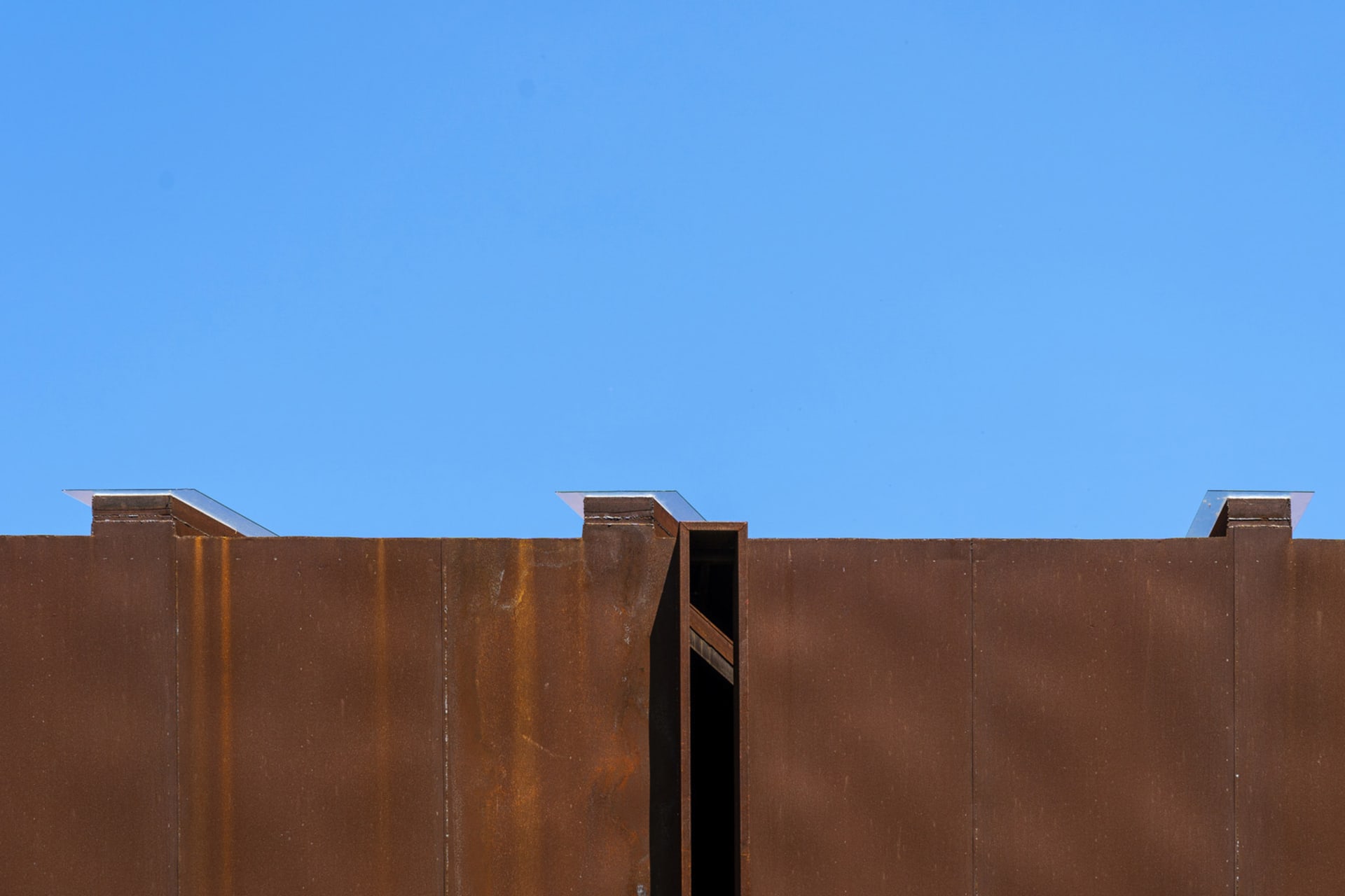 A modern building with a brown roof and a large metal window on its side, set against a clear blue sky
