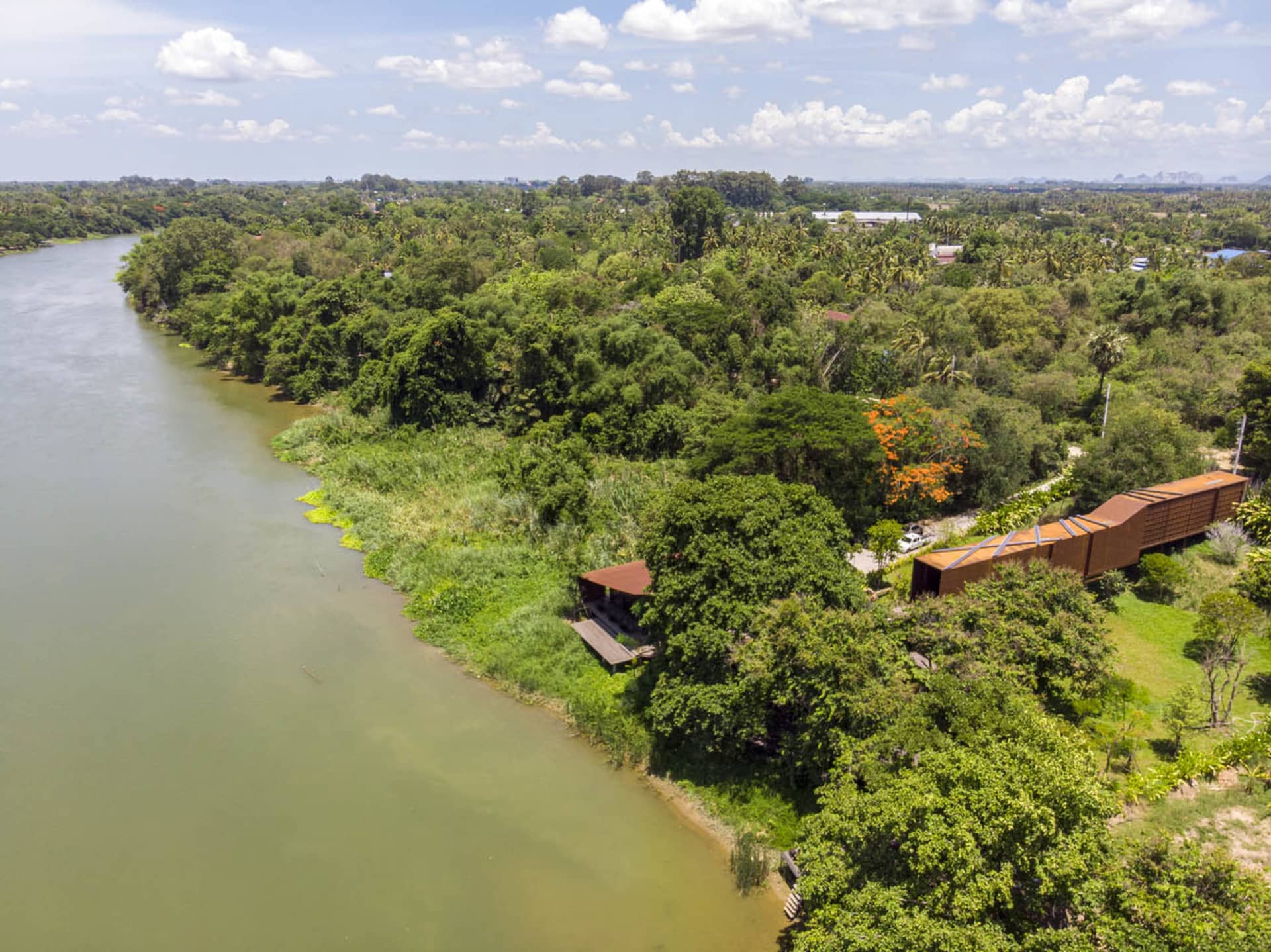 A house with a wooden exterior situated near a river, surrounded by greenery and natural beauty