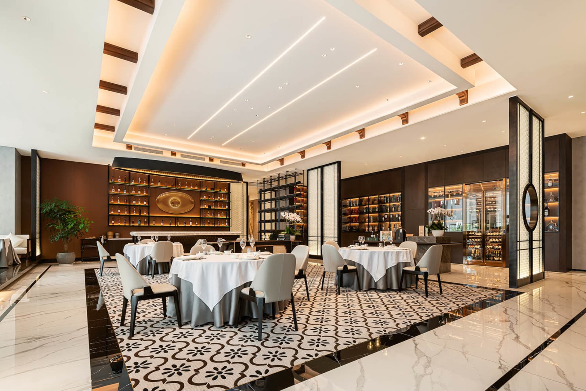 Modern restaurant interior with marble flooring, black and white decor, potted plants, and dim lighting