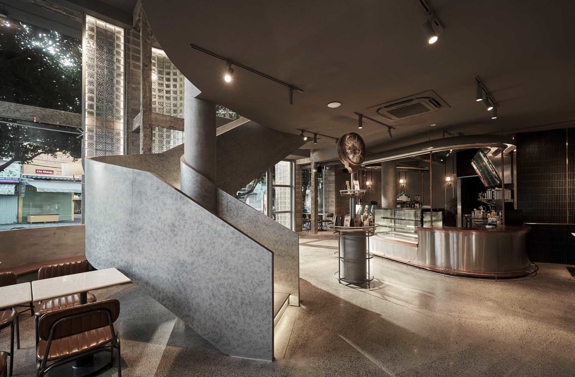 Modern lobby with a staircase, chairs, a dining table, and a clock, set against a well-lit background