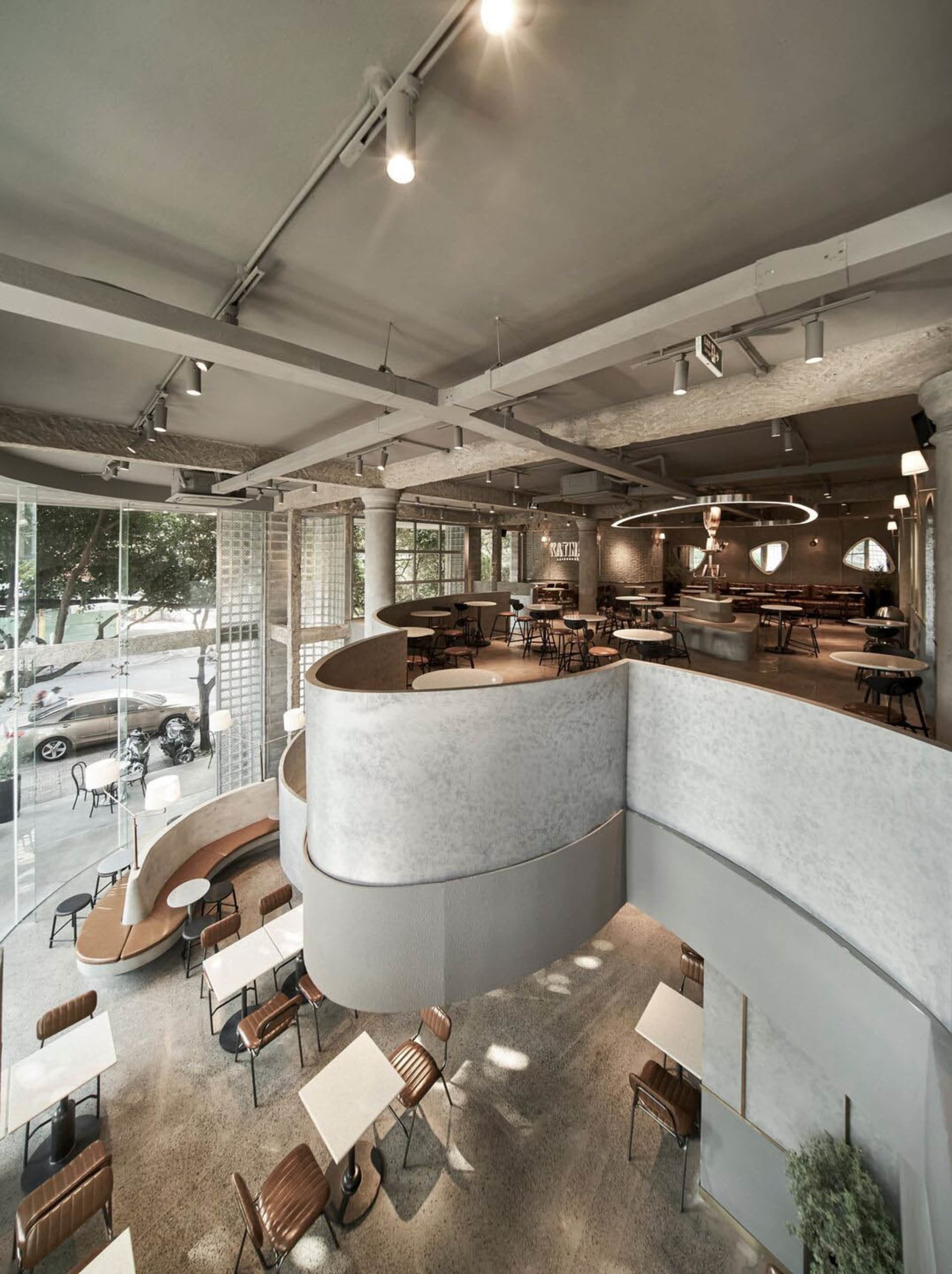 A lively restaurant interior with multiple tables, chairs, and benches, featuring white and grey walls and well-designed lighting