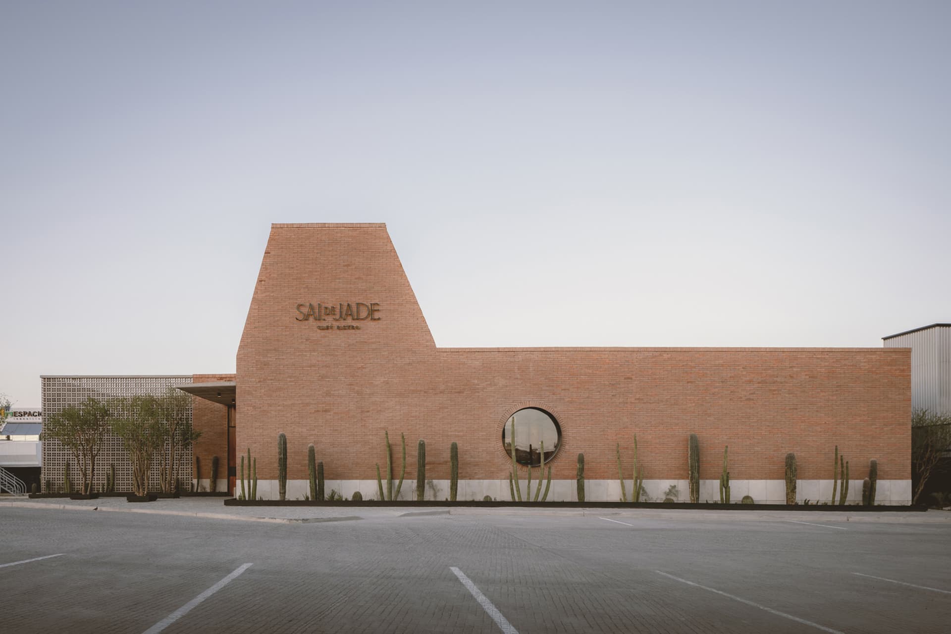 A modern building with a large brick wall and triangular shape, surrounded by cacti in a desert environment