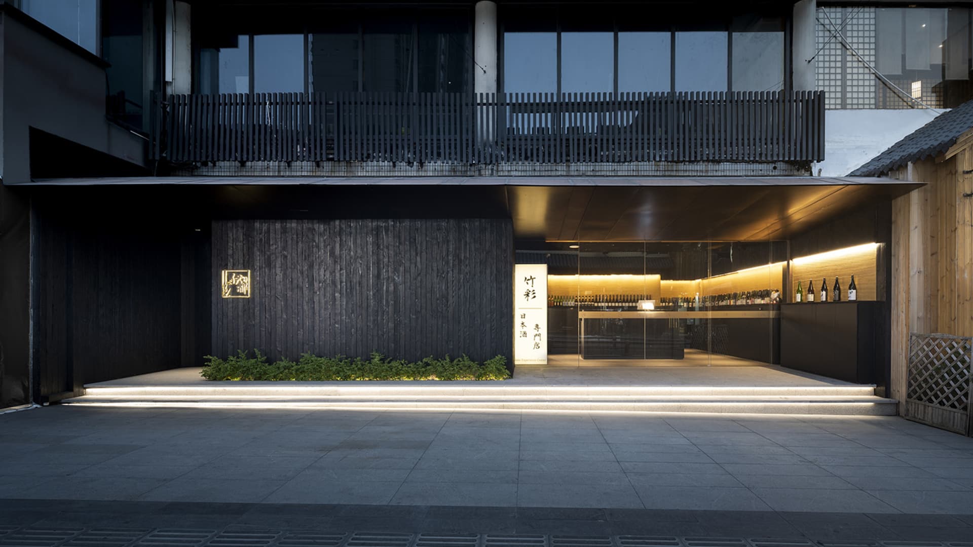 現代亞洲餐廳，黑色立面搭配玻璃前門，寬敞內部設有展示酒瓶與盆栽的酒吧區