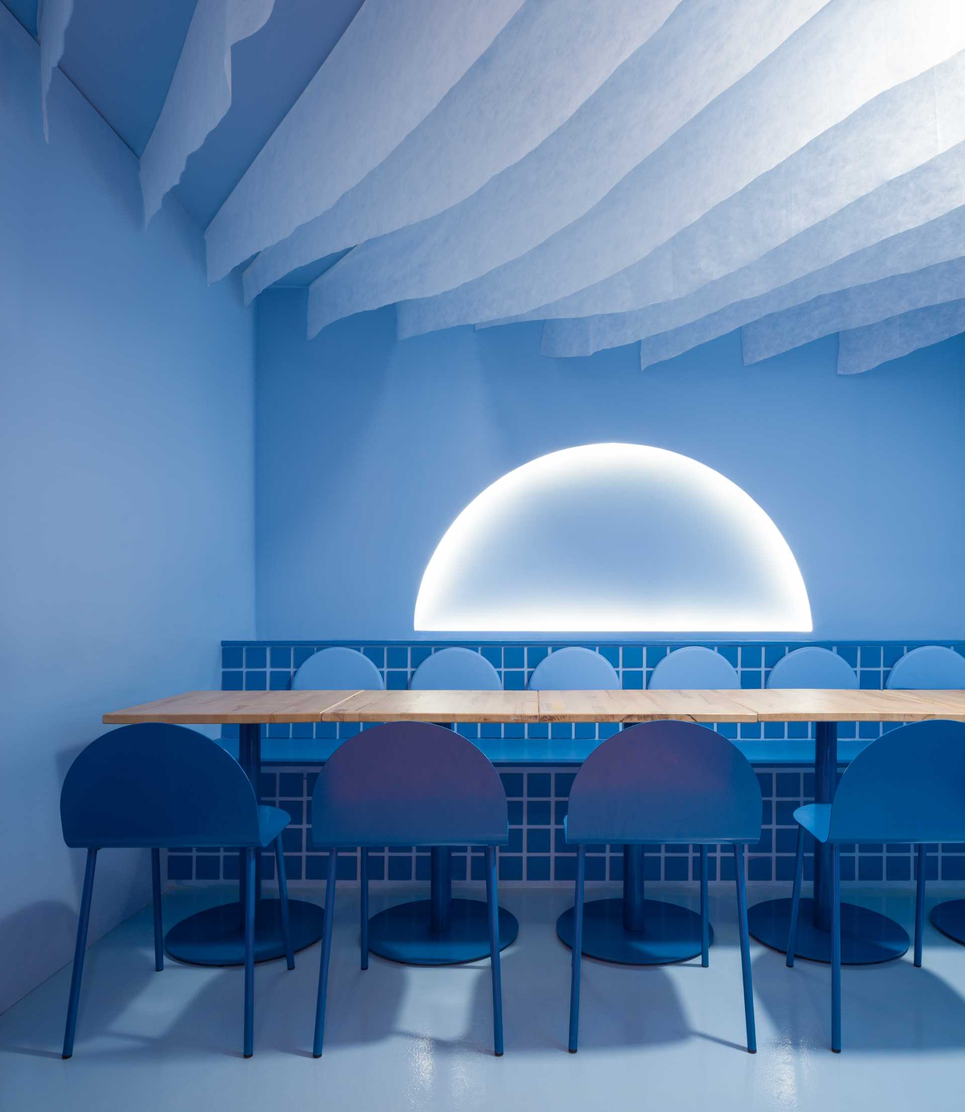 Modern dining space with a large round table and chairs, blue surface, and inviting atmosphere