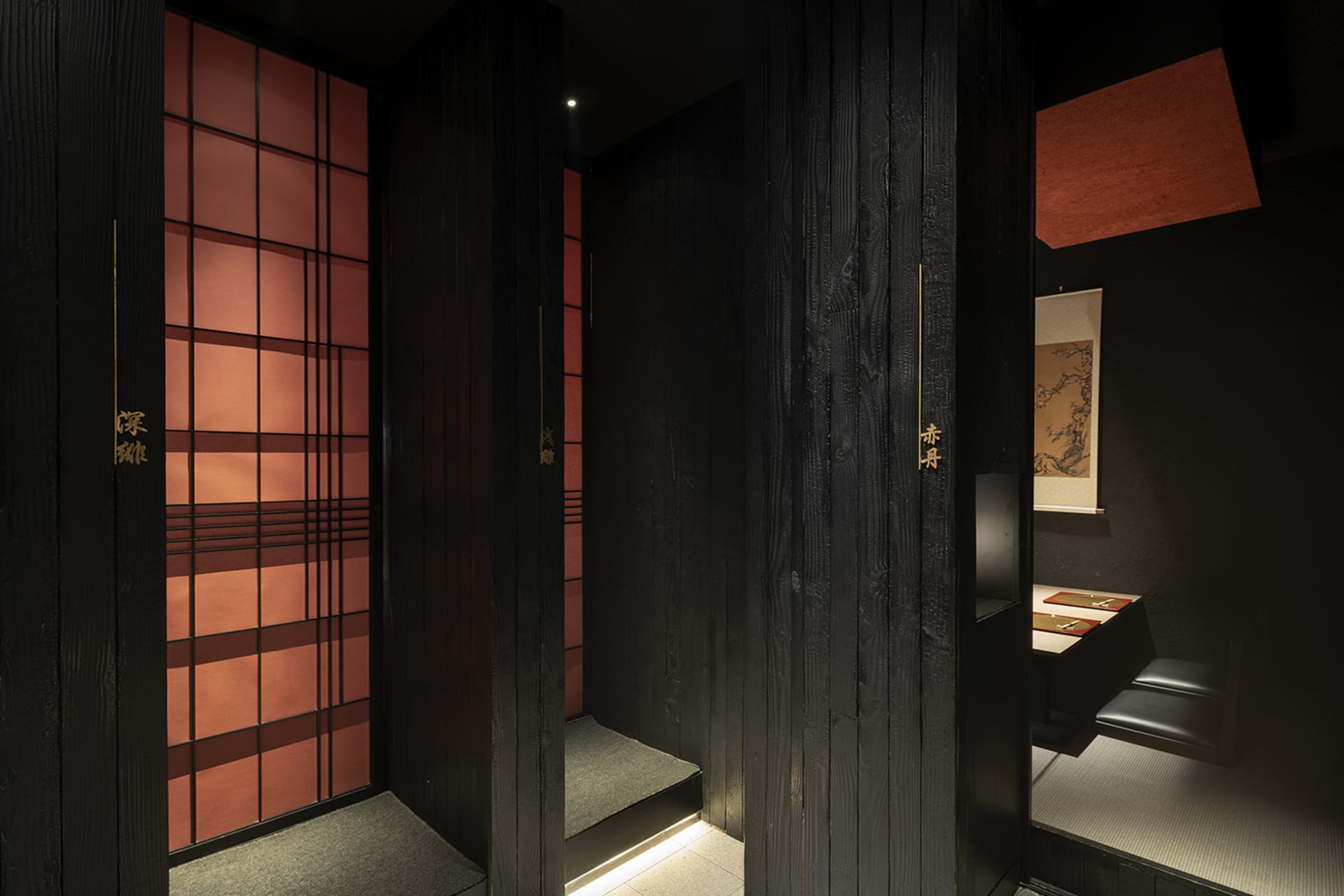 A black wooden door with gold accents in an Asian-style bathroom with a red tiled wall