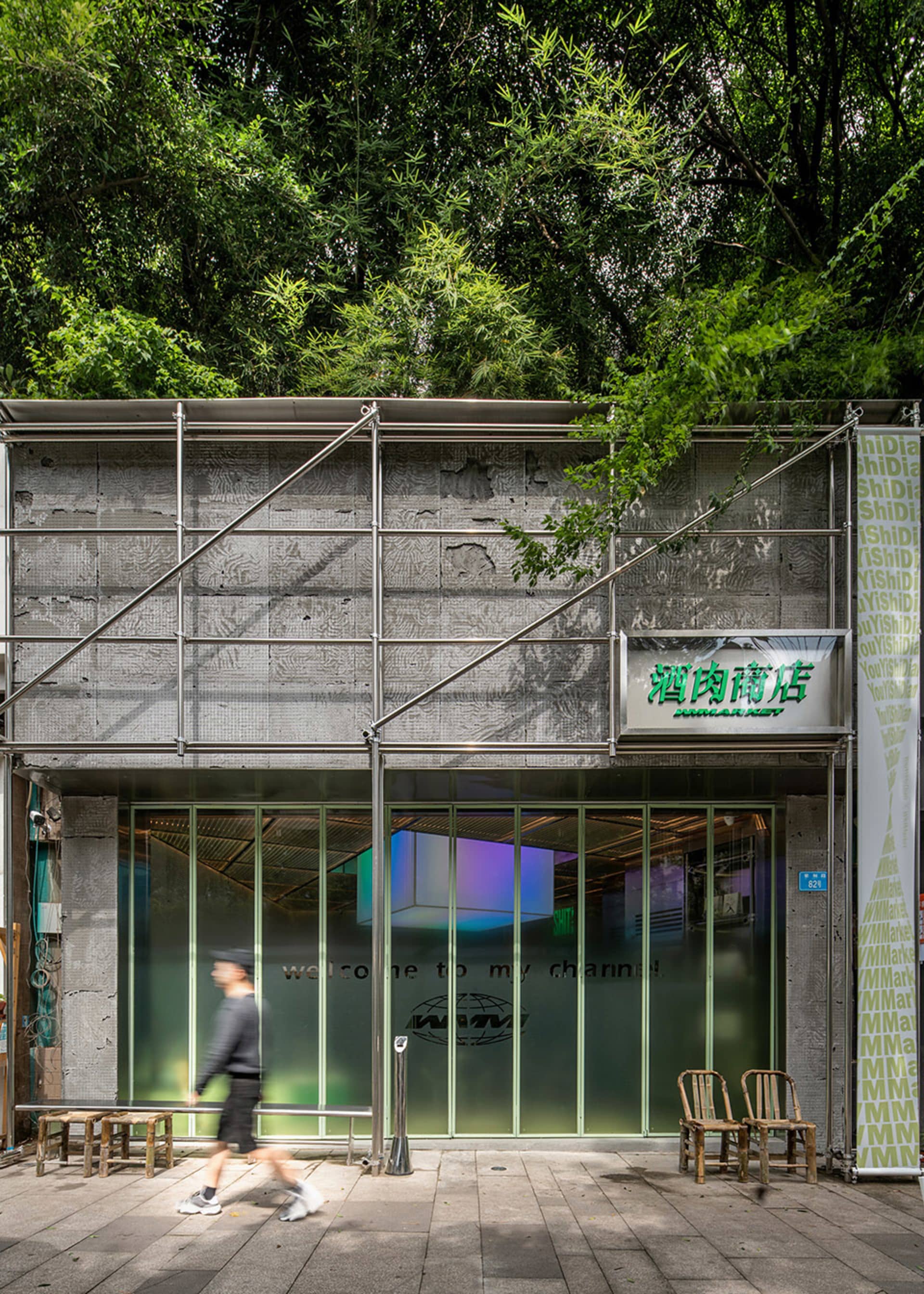 A storefront with a large glass window displaying merchandise, two chairs outside, and a person walking by