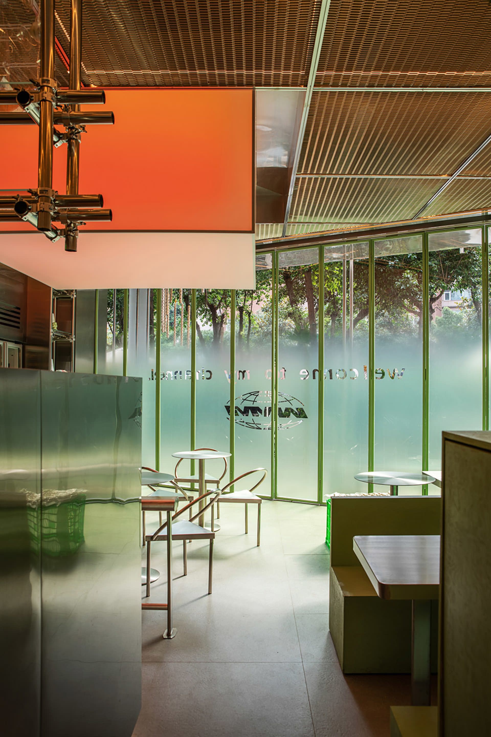 A modern restaurant interior with green glass walls, natural light, and comfortable seating areas