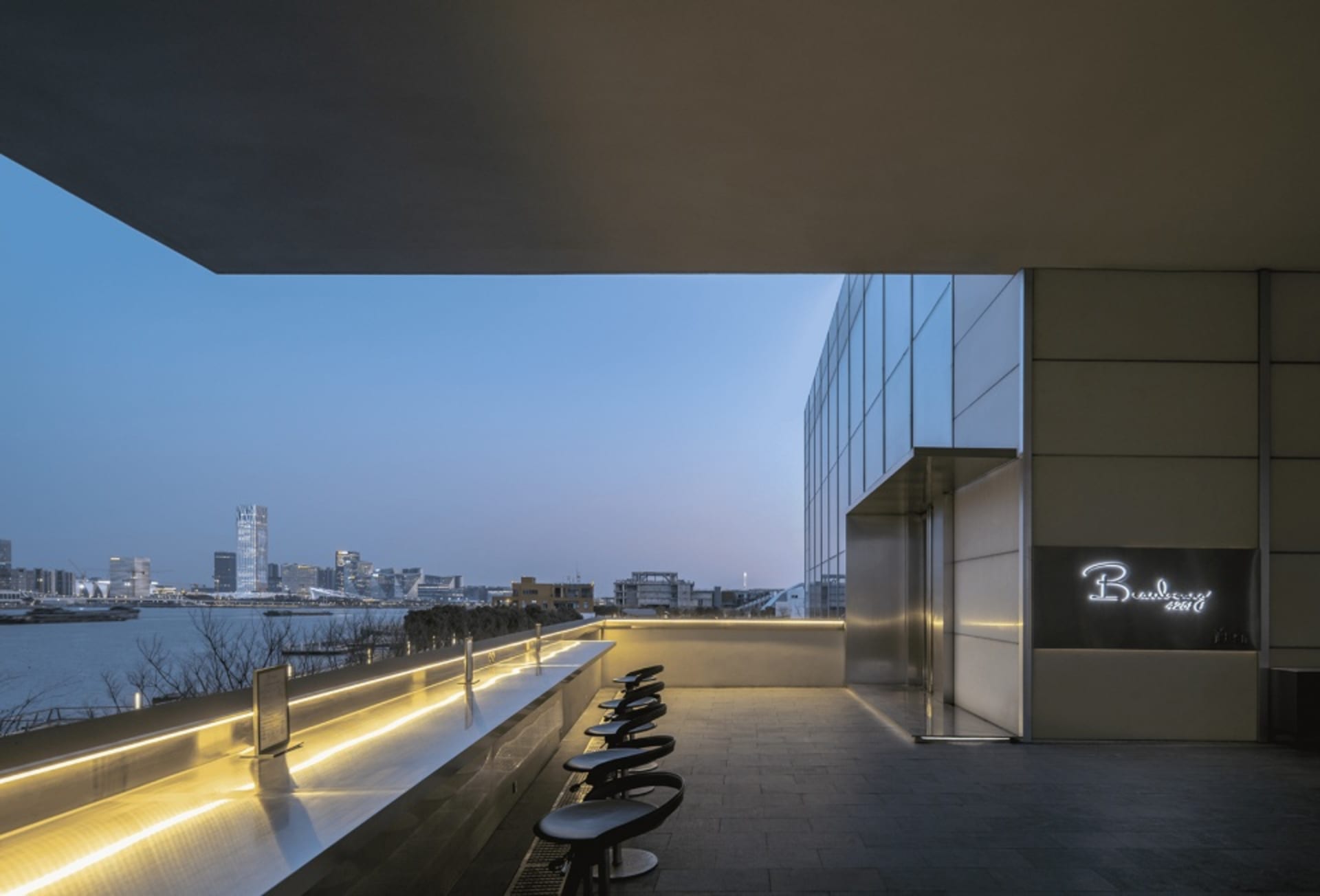 Nighttime exterior view of a modern building with a large glass wall and chairs in front, providing a sleek and functional atmosphere