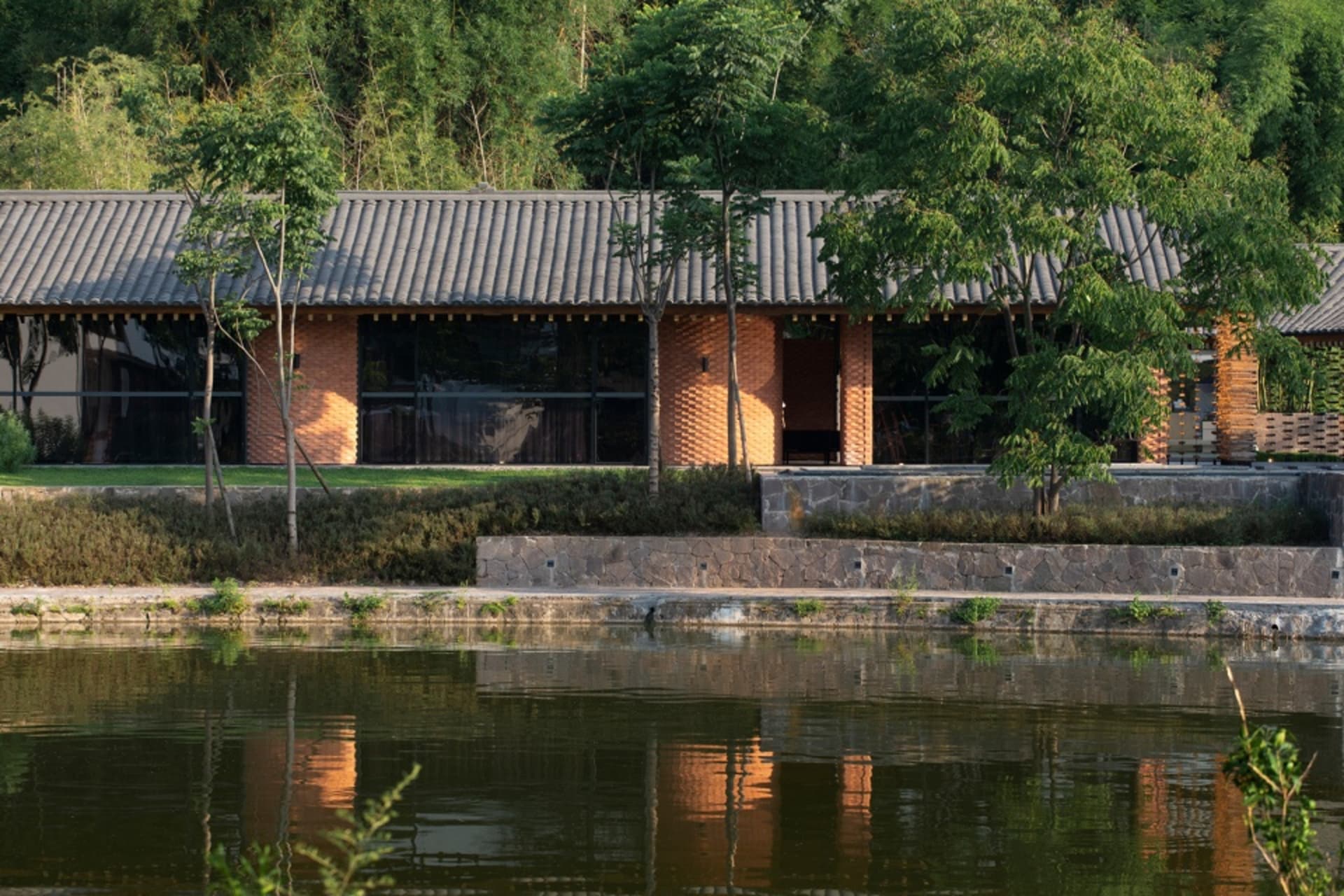 Asian-style house near water with a large wooden structure, multiple windows, and outdoor furniture