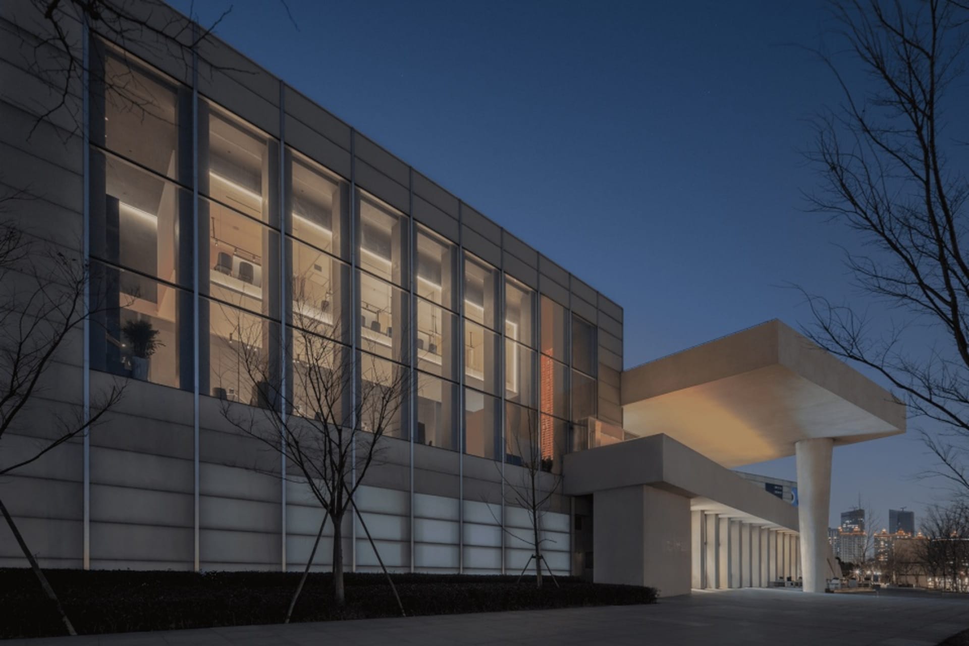 A modern building with a glass structure and concrete exterior, featuring many windows and outdoor seating areas