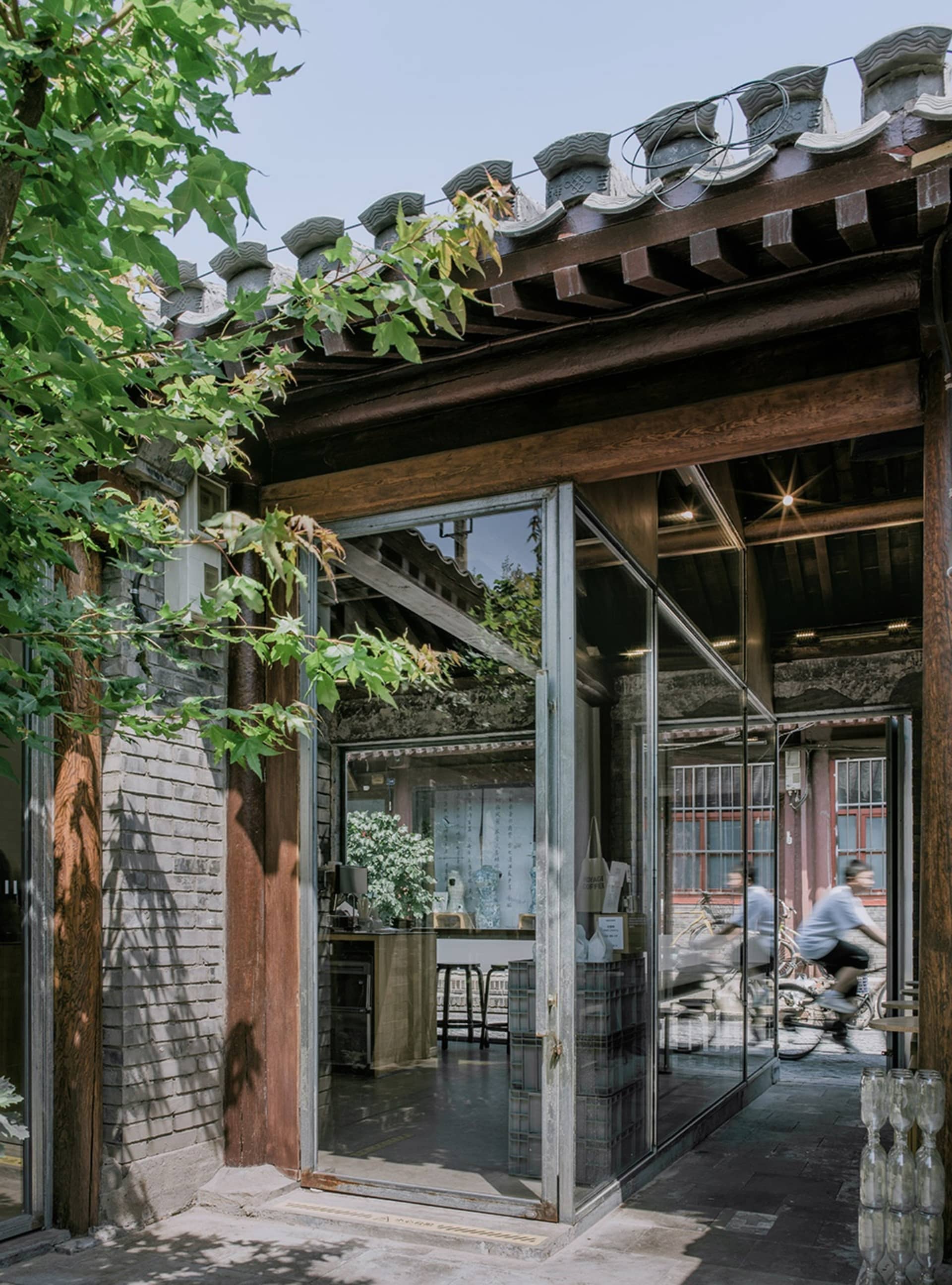 Asian-style living room with a wooden exterior, featuring a large open area with chairs and a bicycle, and a glass door leading outside, with natural light streaming in through the windows