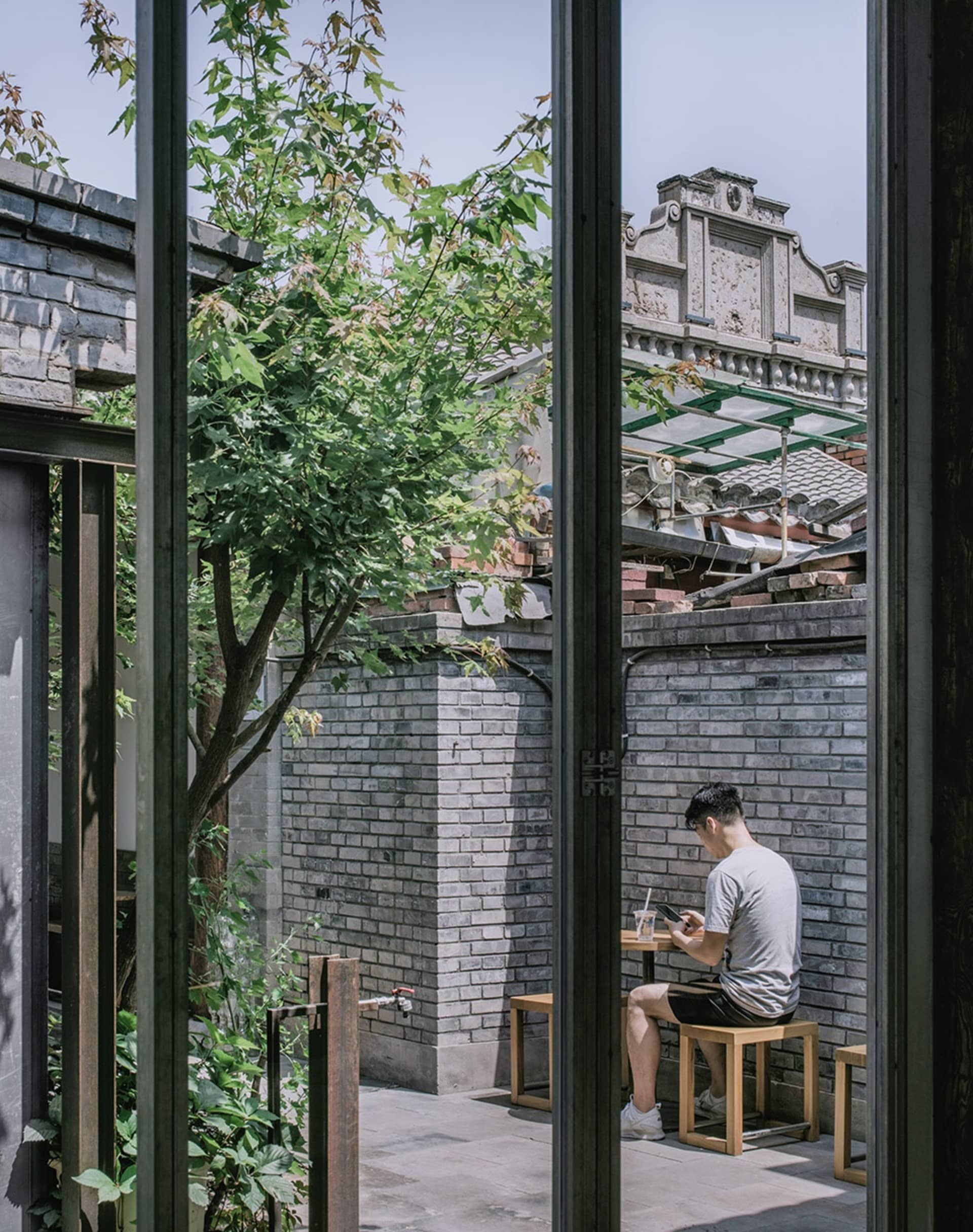 一名男子坐在戶外餐桌旁，周圍環繞木椅與桌子上擺放的碗，這是餐廳或戶外用餐區