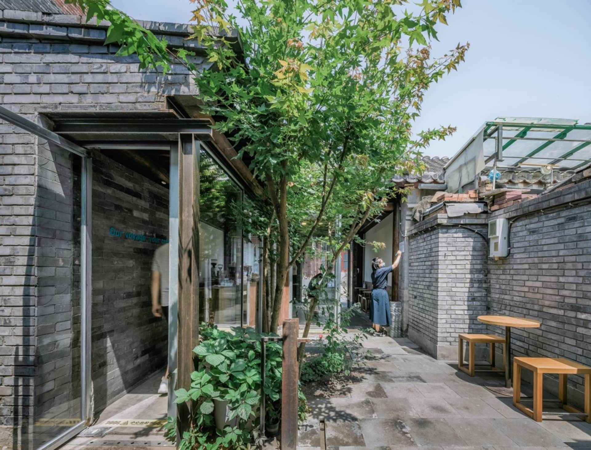 磚牆立面與露台的鄉村風住宅，設有餐桌、沙發及盆栽，場景中有人物