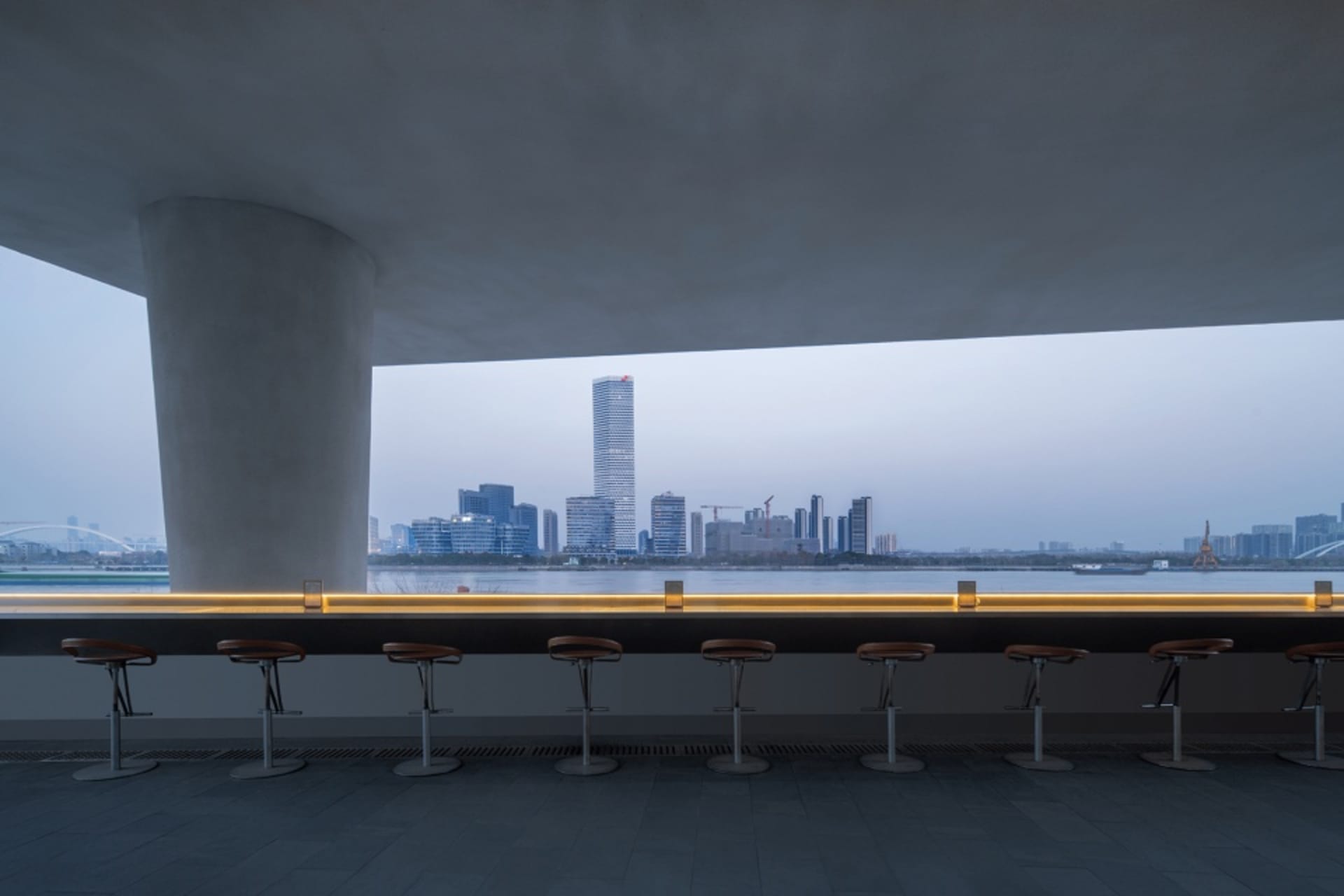 Modern restaurant bar with stools and chairs, overlooking a city skyline, with warm and inviting lighting